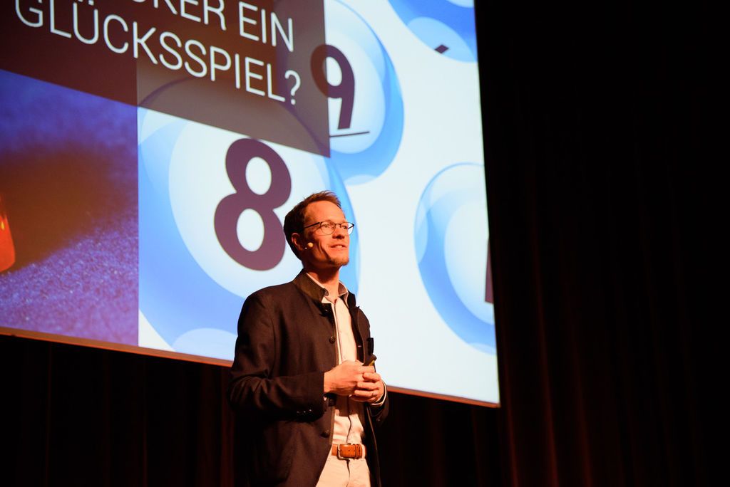 Ein Mann hält einen Vortrag vor einer Leinwand mit der Frage, ob Poker ein Glücksspiel ist