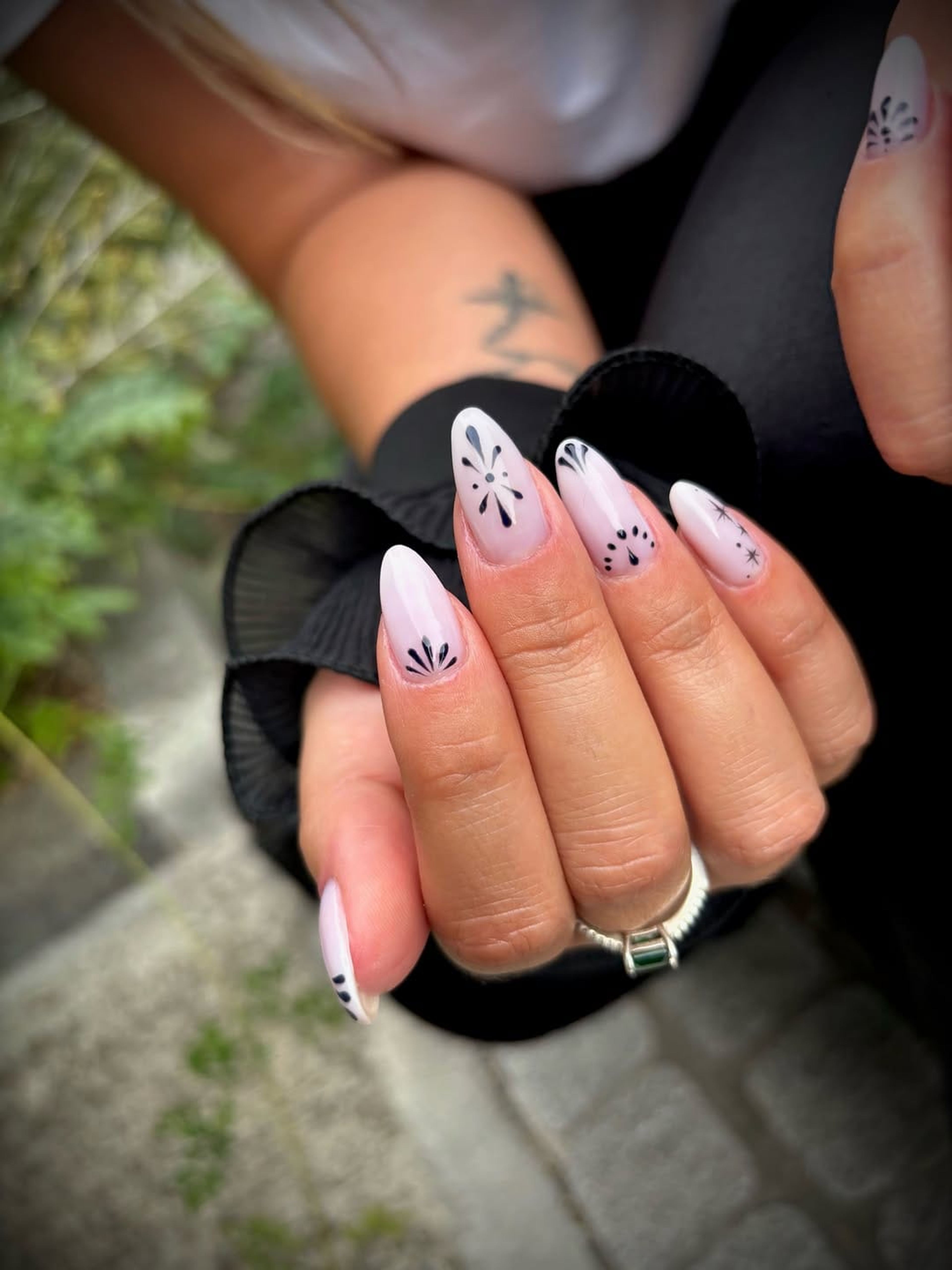 Deux mains aux ongles blancs ornés de marguerites noires, en extérieur.