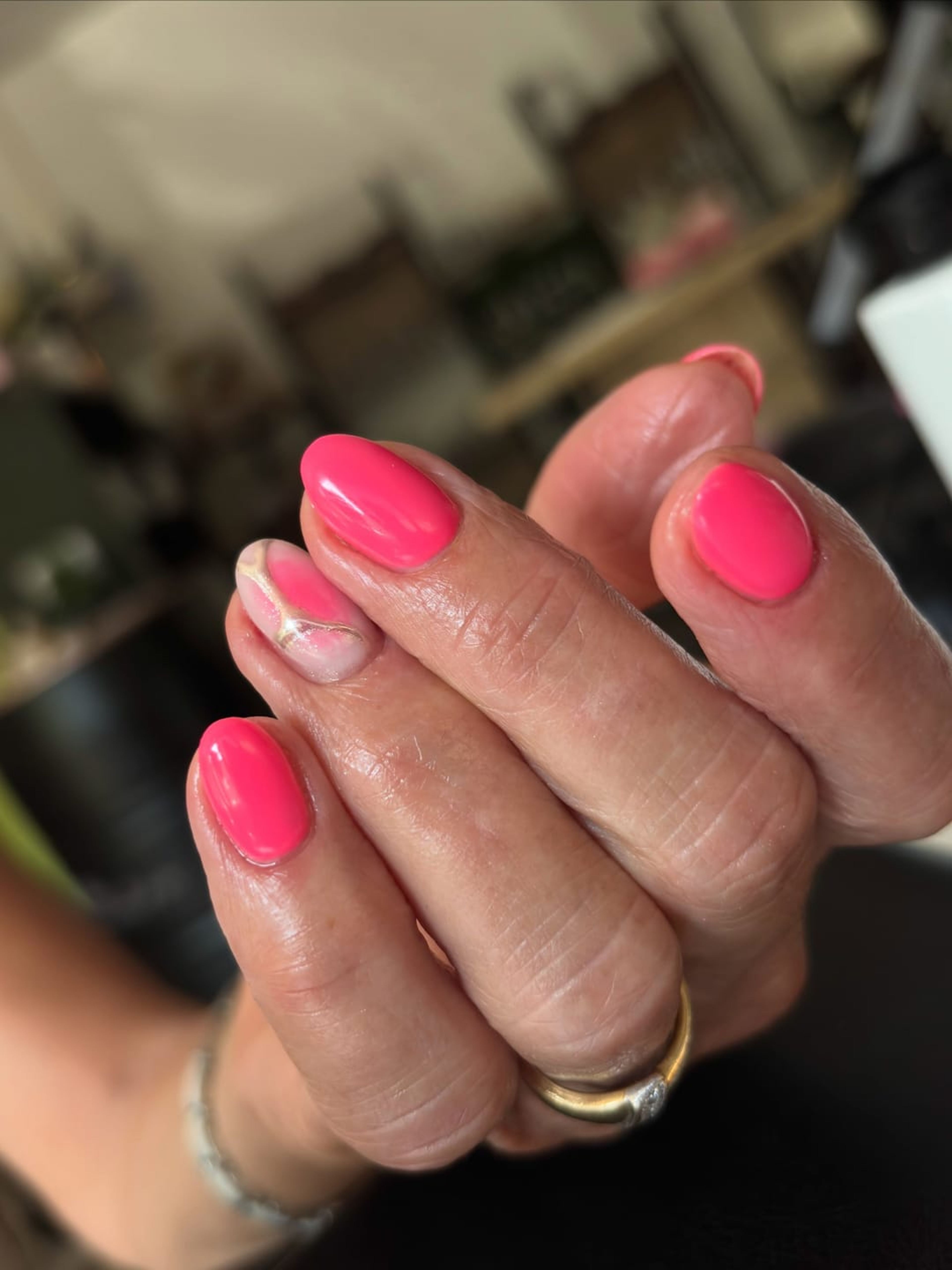 Main aux ongles framboise brillants, dans la lumière d’un salon.