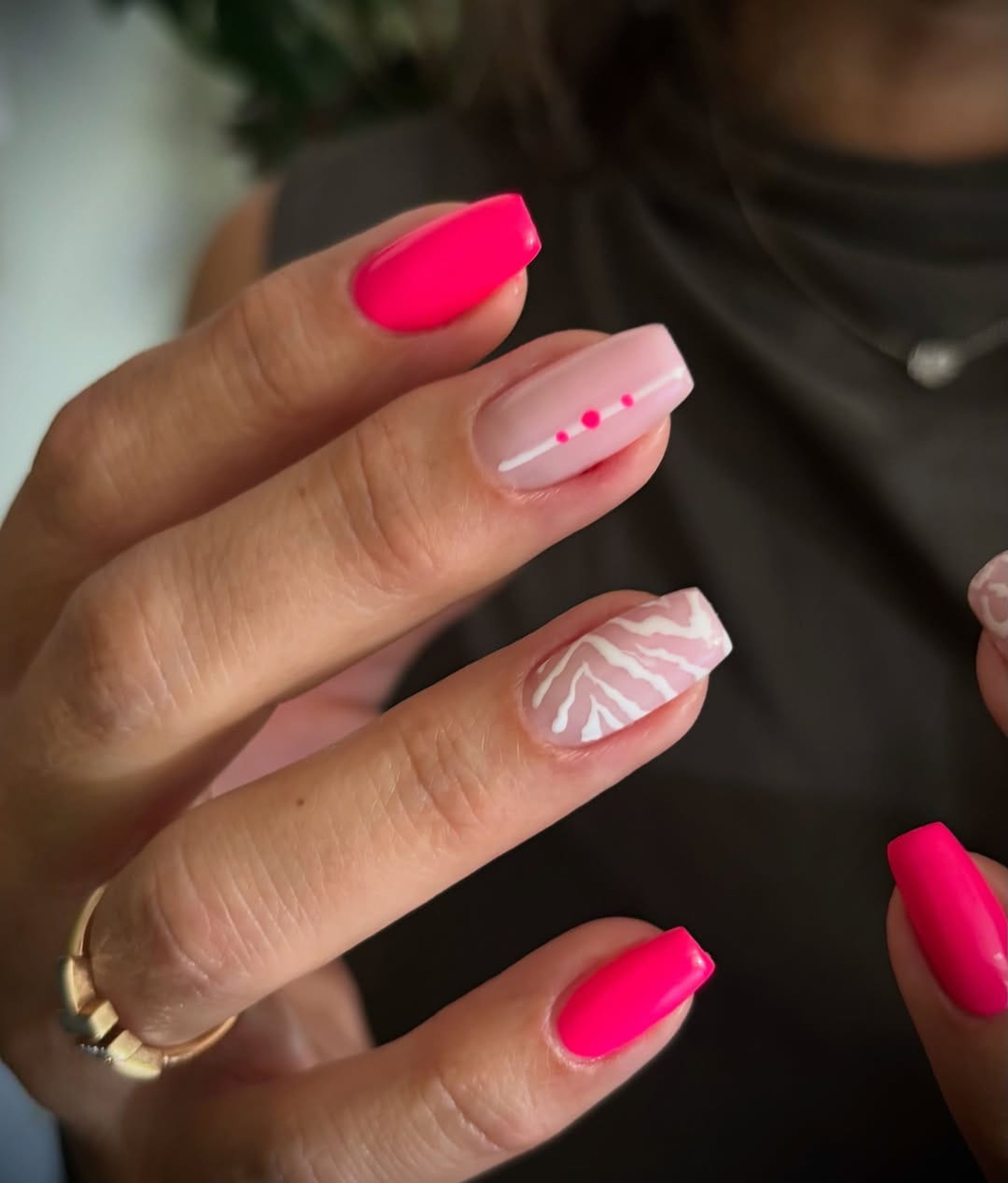 Main aux ongles fuchsia et rose pâle, avec un motif blanc peint sur deux doigts.