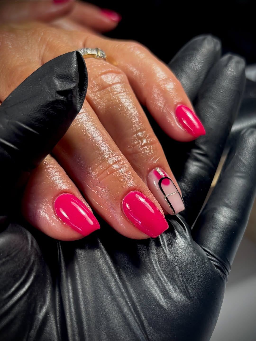 Main aux ongles fuchsia brillants tenue par une main gantée de noir, en cabine.