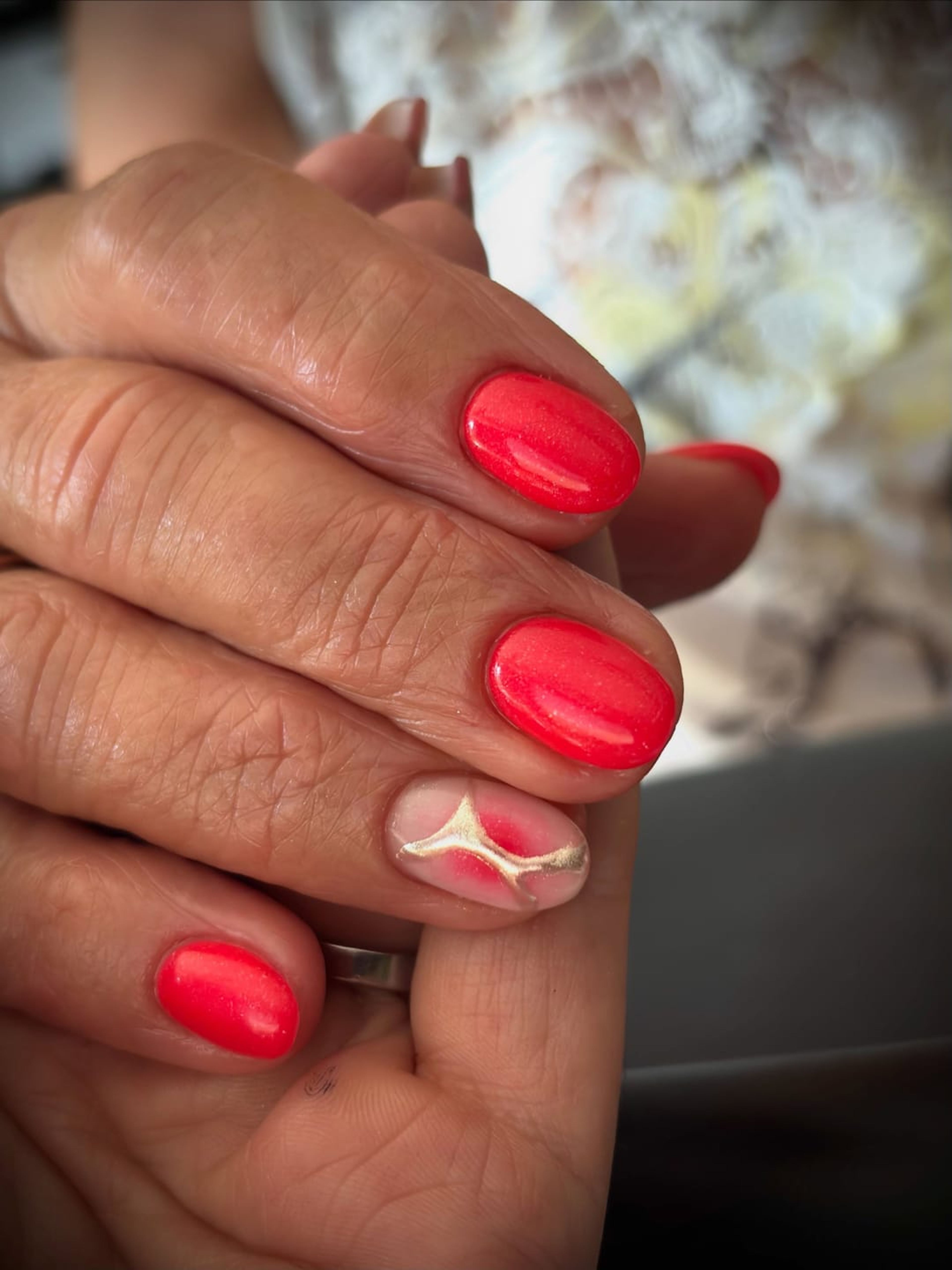 Mains croisées, ongles rouges brillants, devant un fond fleuri flou.