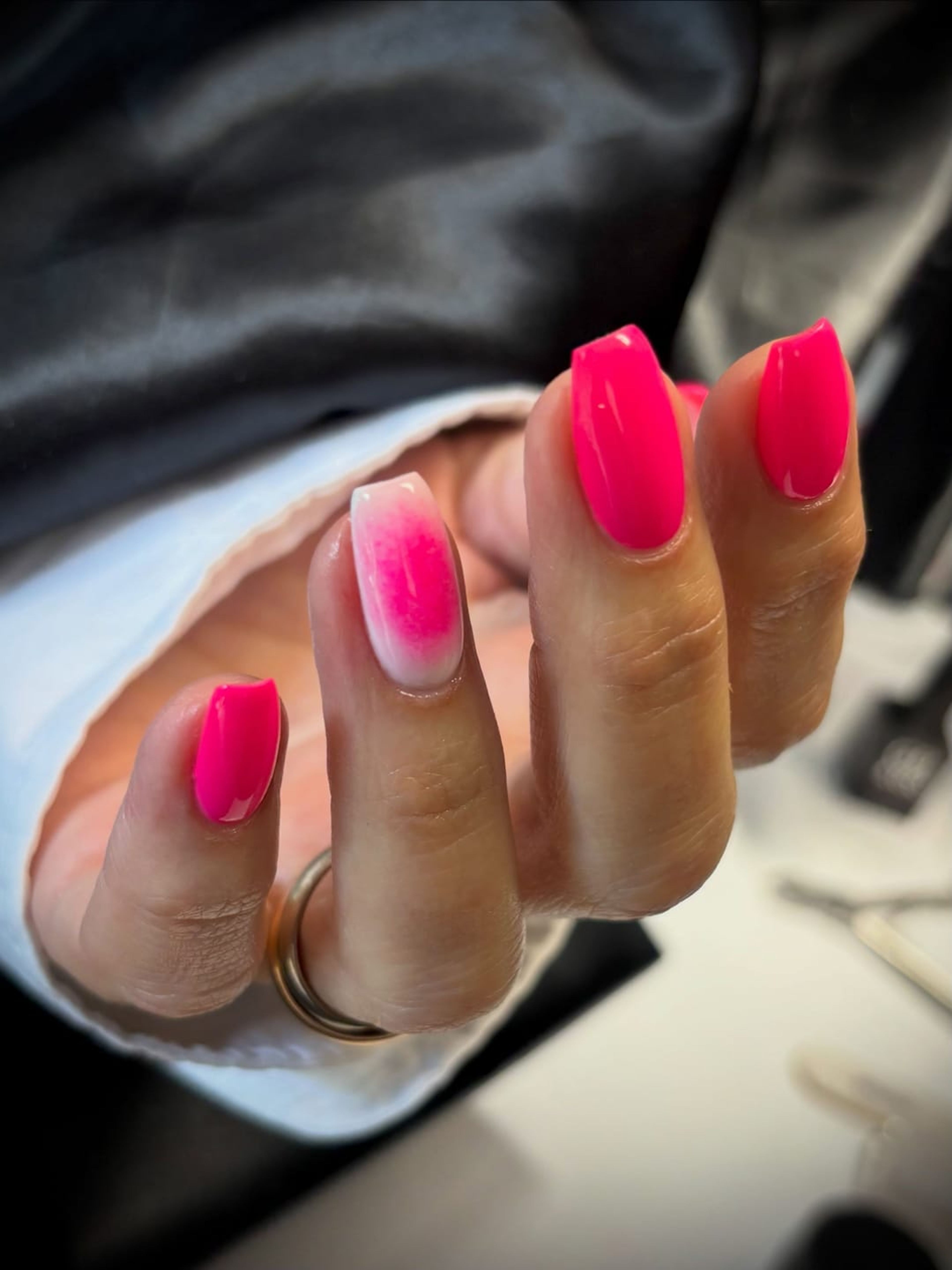 Main aux ongles fuchsia et dégradé rose, manche claire sur fond sombre.