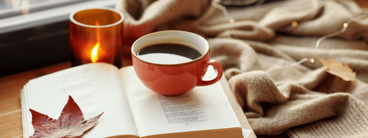 Mug of coffee on an open book and warm, soft blankets, highlighting soft rituals
