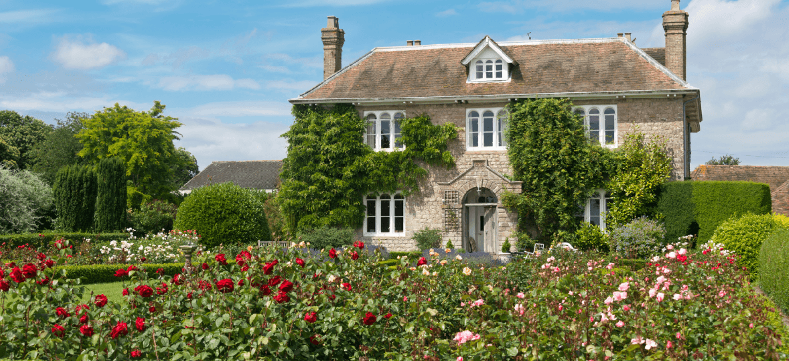 Home stewardship example with country house, maintained garden and structured planting in bloom