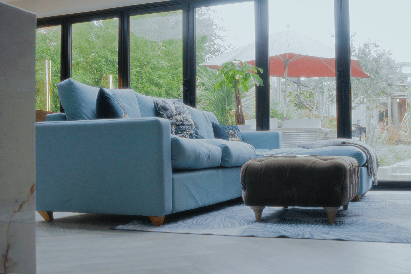 Beckenham home interiors living room with blue sofa, ottoman and garden view through sliding doors