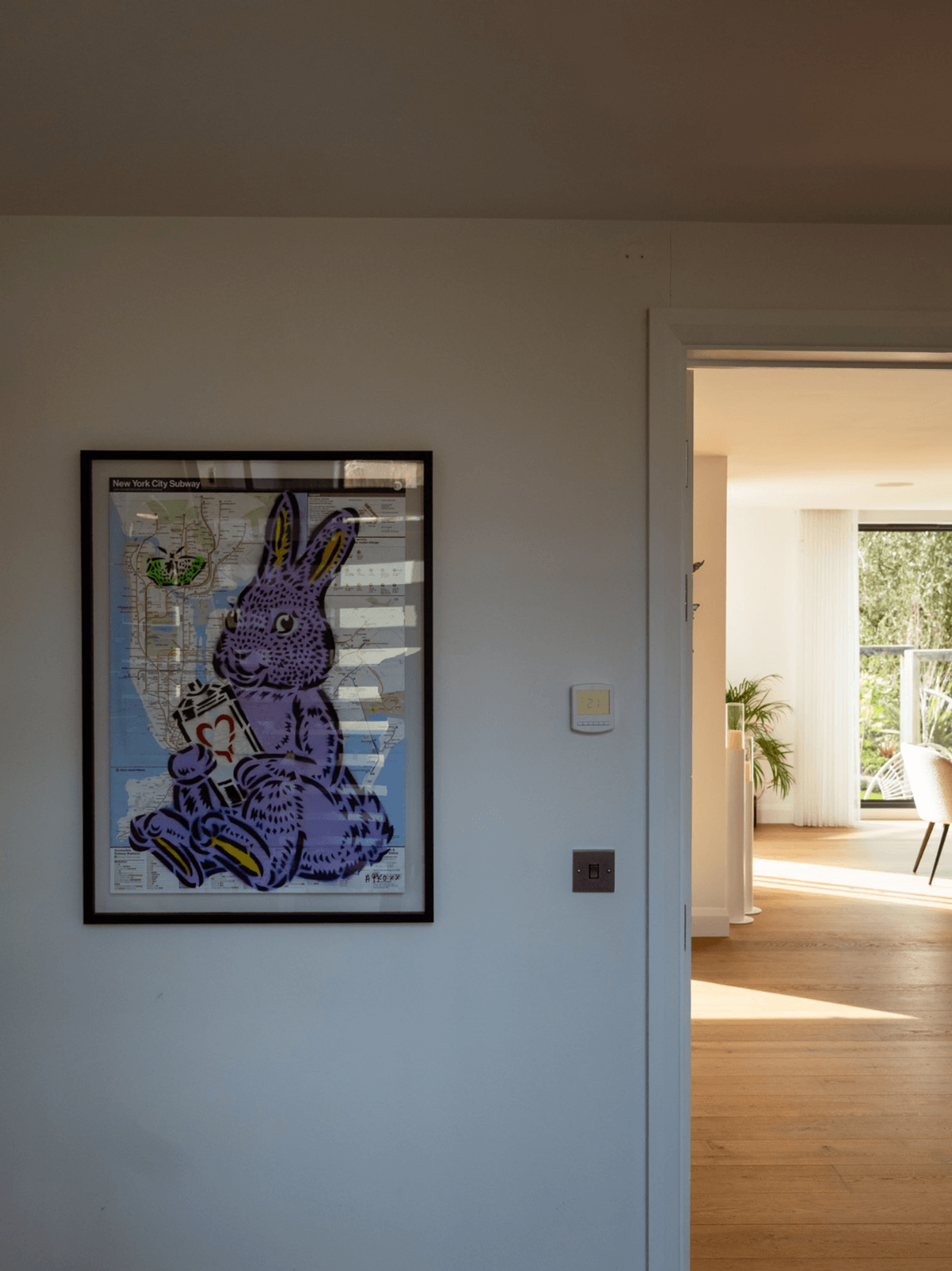 Sevenoaks interior design hallway with framed rabbit artwork over New York subway map and light-filled adjoining room