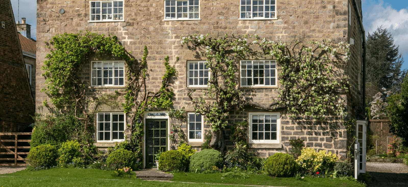 Home stewardship example with traditional stone cottage, climbing plants and well-maintained front garden