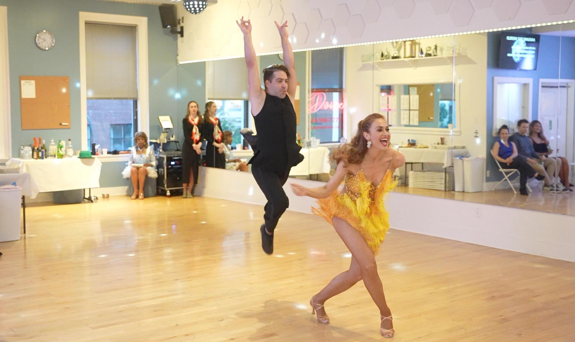 Jerry leaping mid-air behind Vanda, who lunges toward the camera in a yellow fringe dress — jive at a Big Apple Ballroom show.