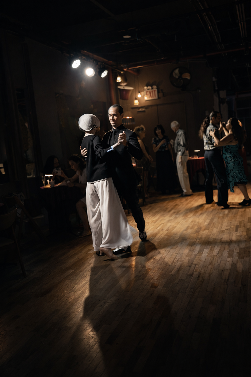 A couple dancing in closed position under a single spotlight on a darkened floor.
