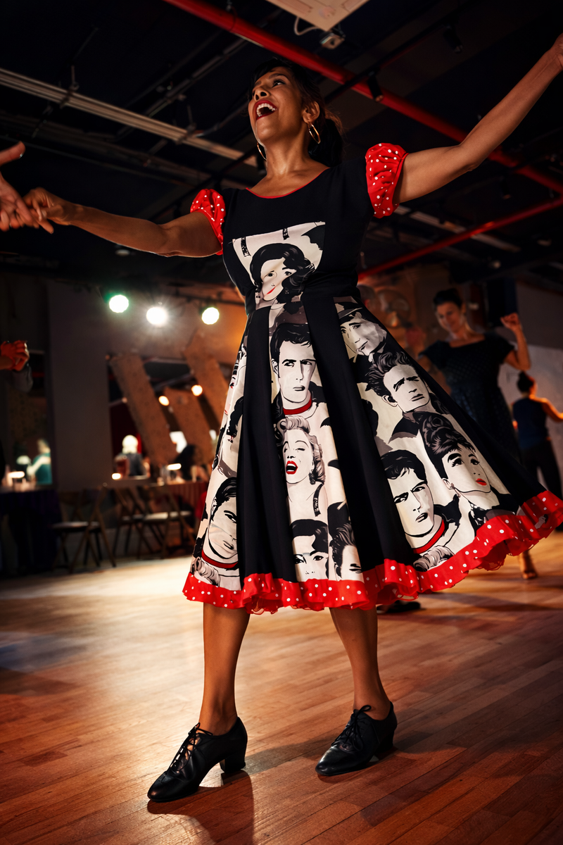 A dancer mid-spin in a full-circle swing dress with red polka-dot trim, arms extended, on the Big Apple Ballroom floor.