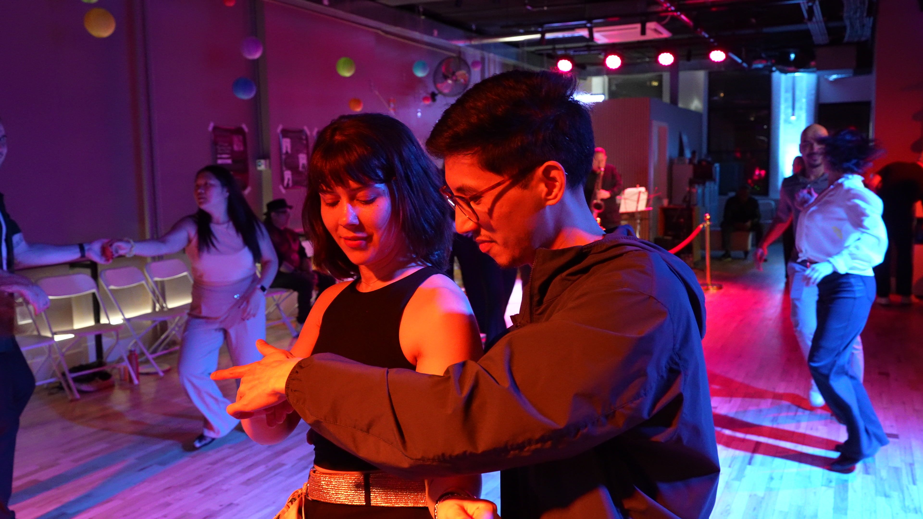 Two dancers in a close hold at a Big Apple Ballroom social night, blue and red light across the floor.