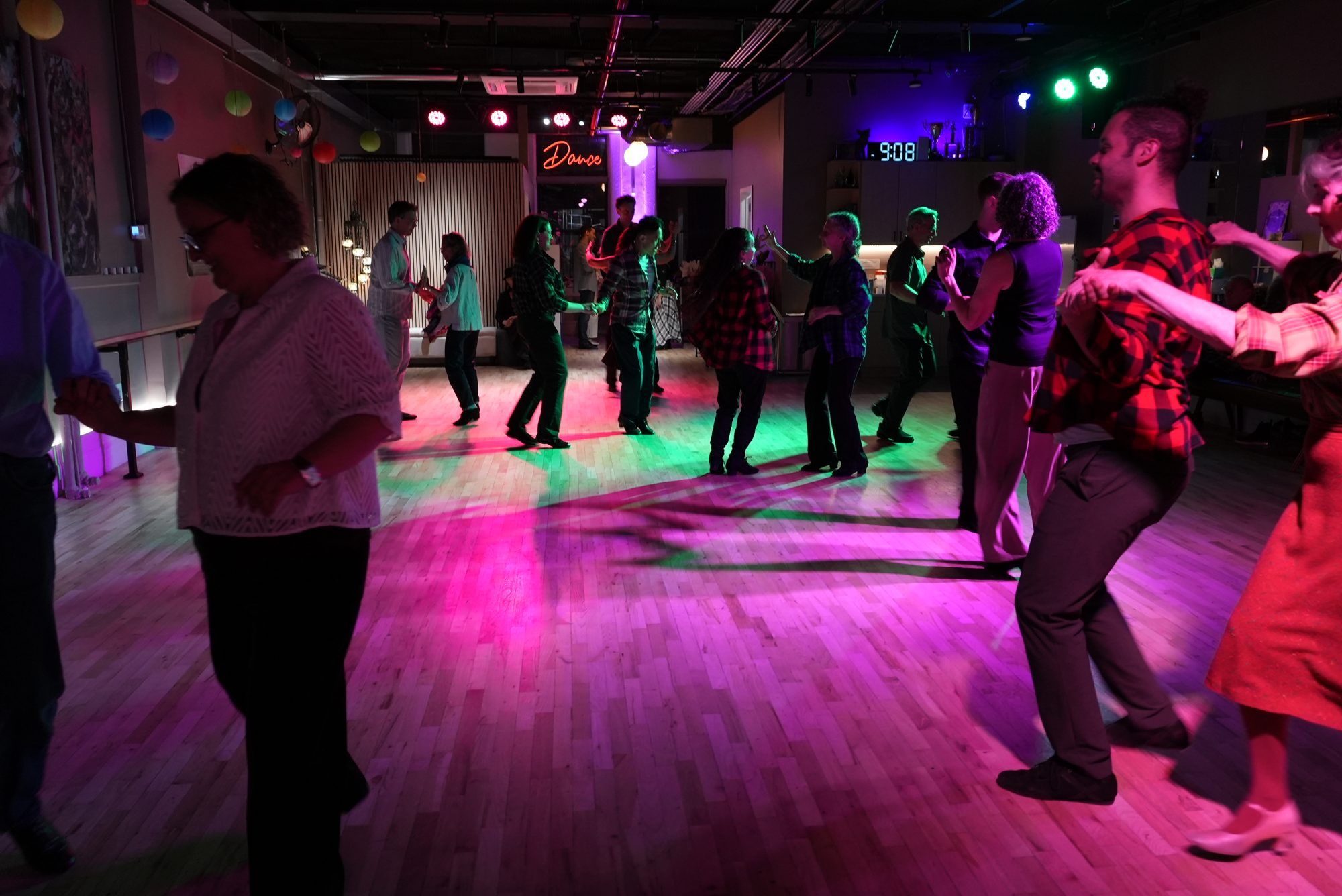 A full dance floor under coloured lights at Big Apple Ballroom, couples dancing after the evening class