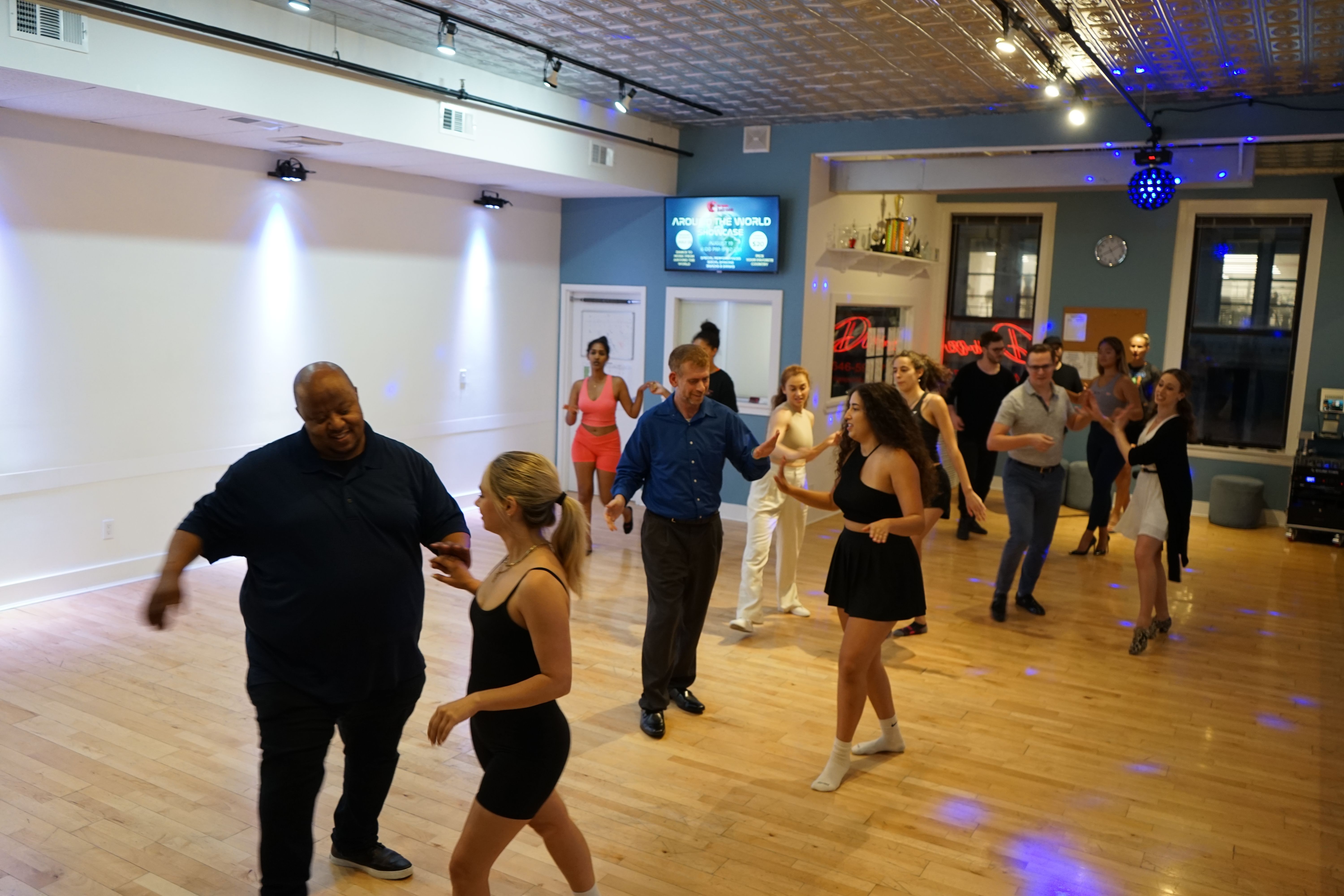 A bright group class at Big Apple Ballroom — students of all ages practicing together on the wooden floor.