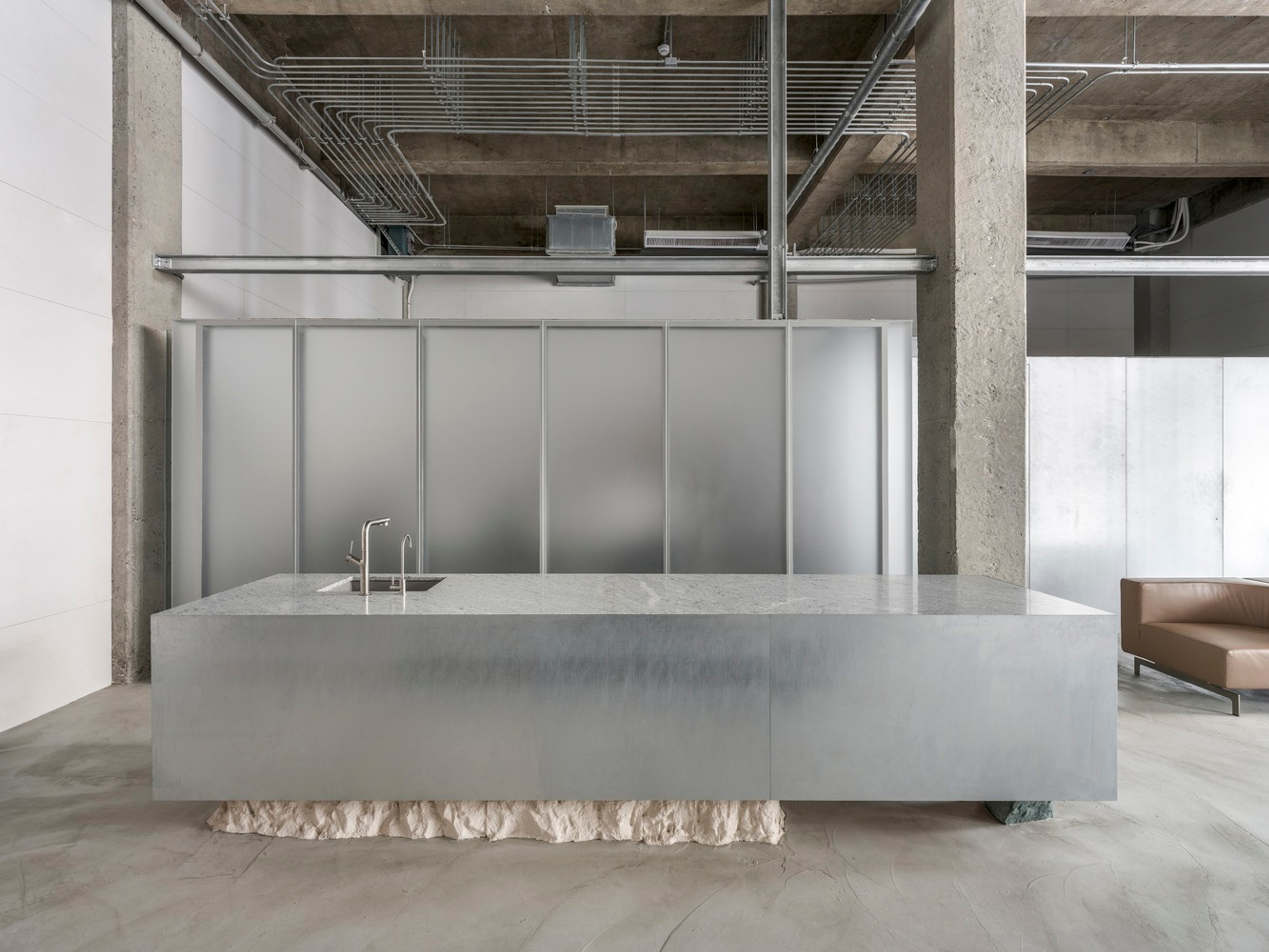 Placeholder reference image: Long metal counter inside an exposed concrete interior with glass partitions.