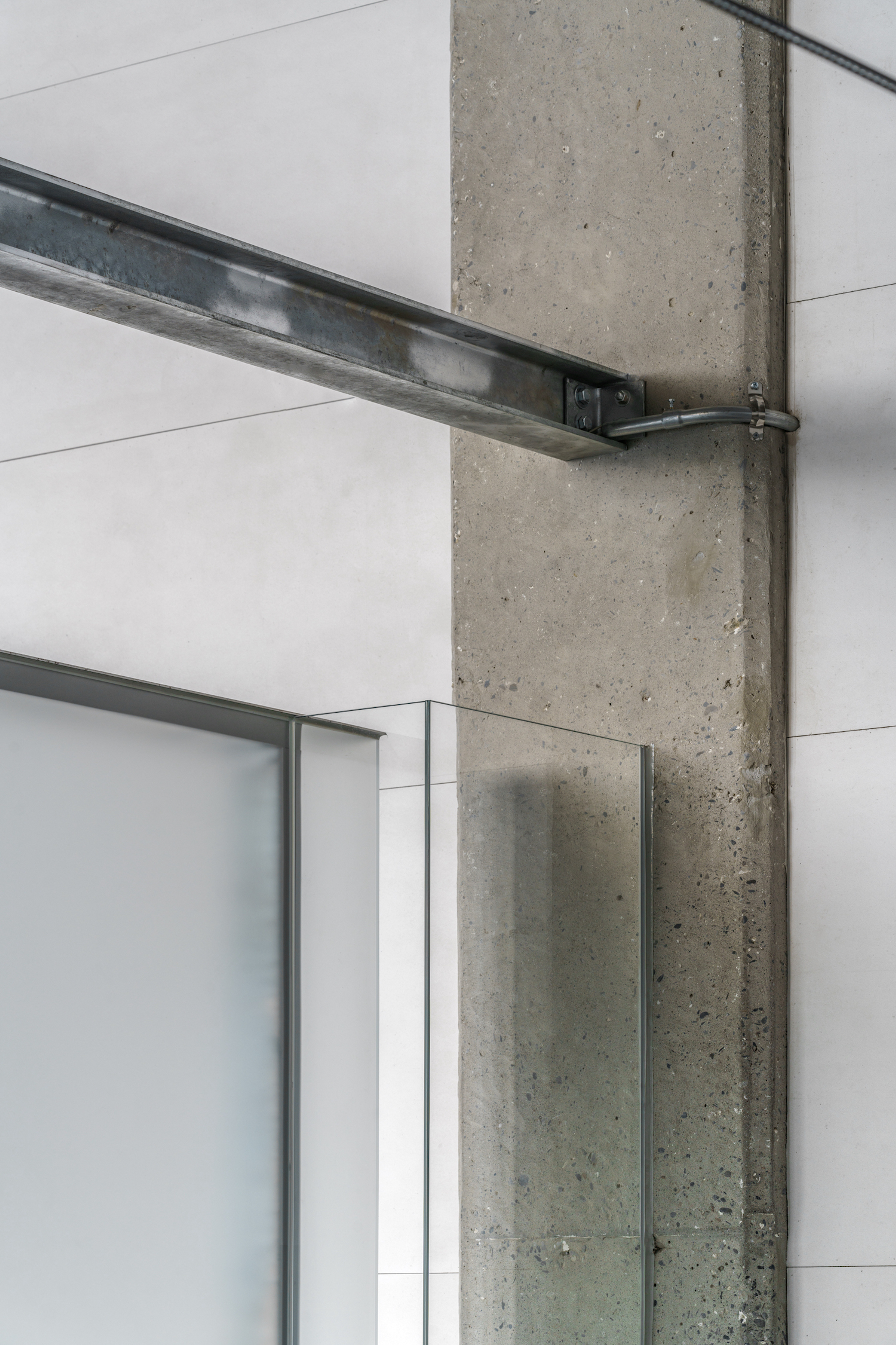 Exposed concrete column with a metal beam connection, glass partition and pale wall panels at Oskay Store.