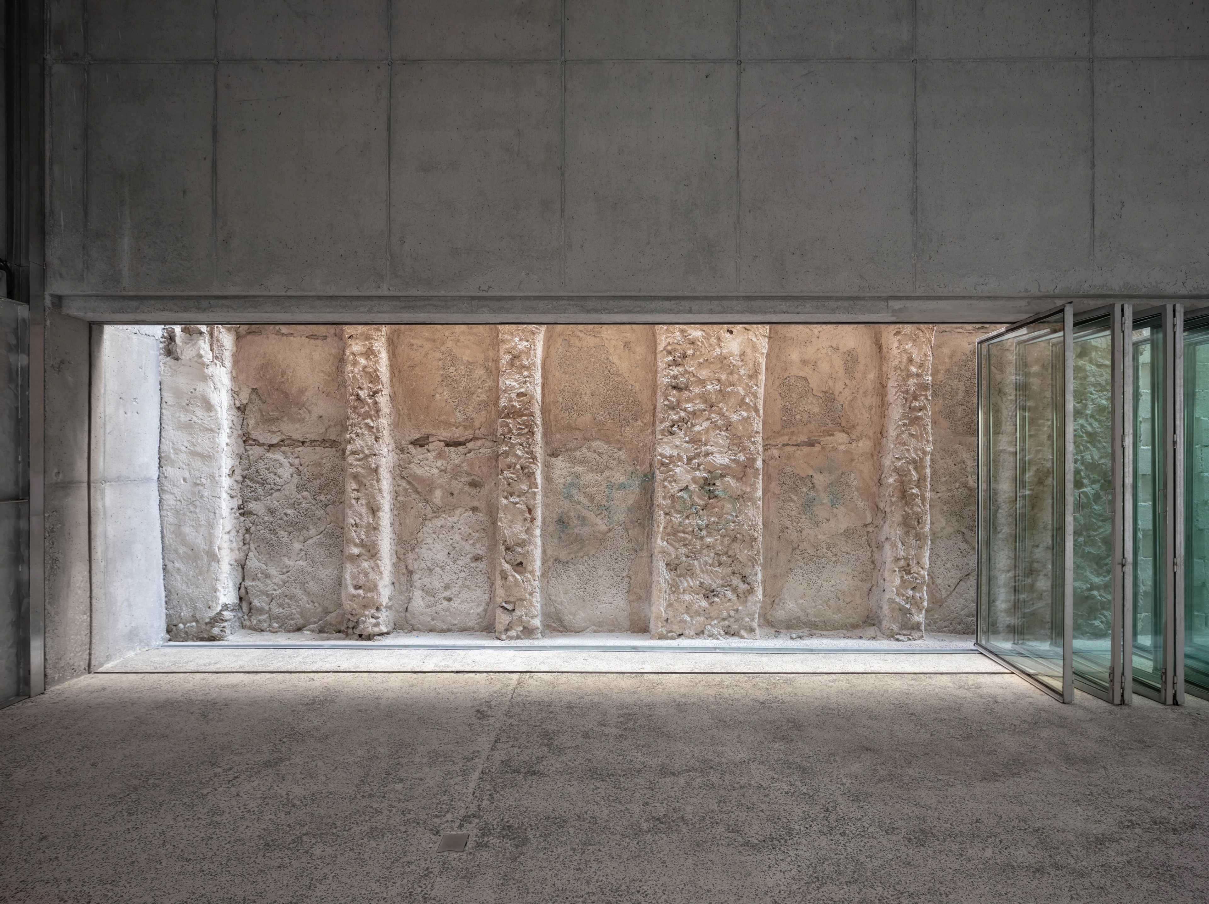 Placeholder reference image: Concrete room with a broad glazed opening facing a rough stone wall.