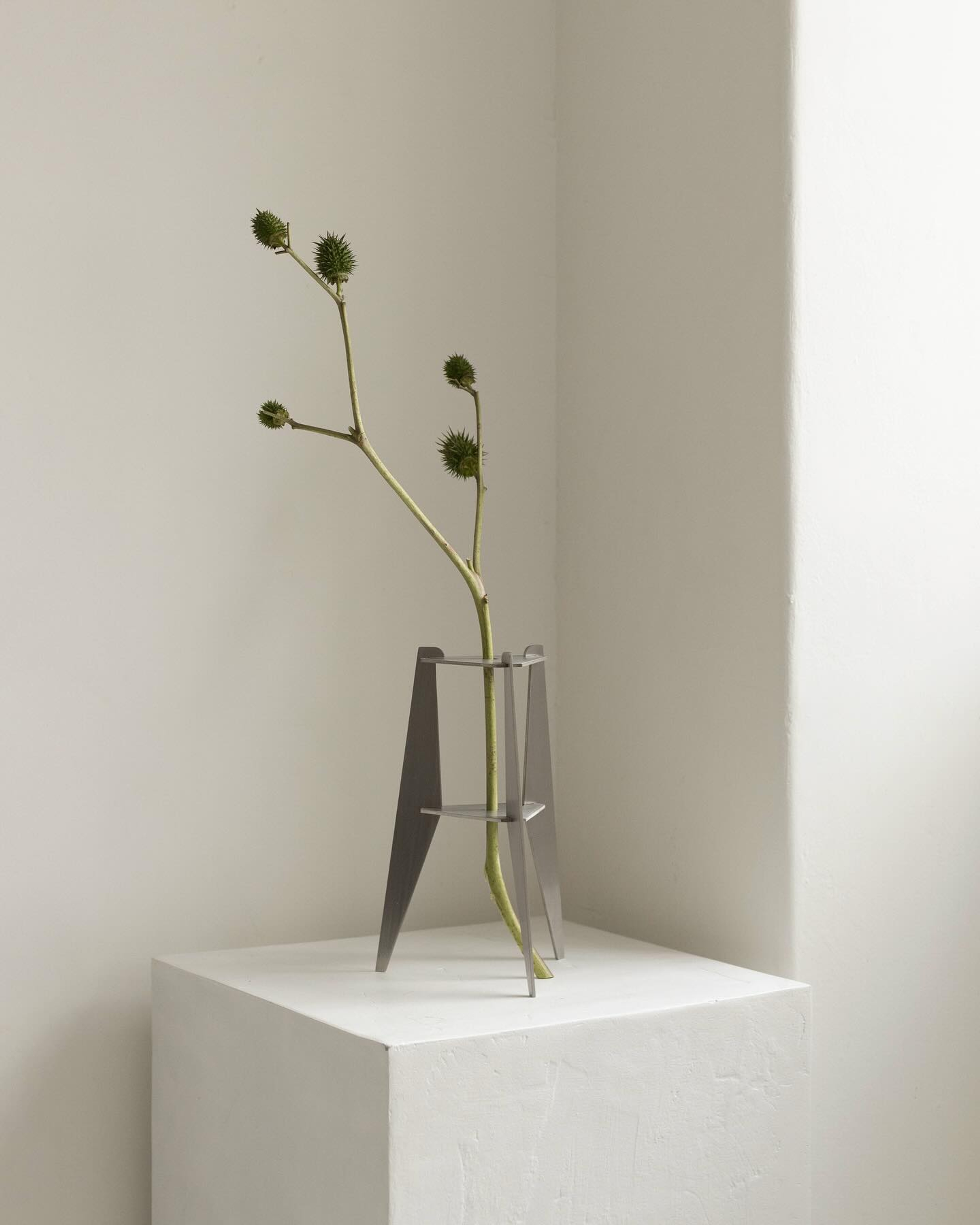 Placeholder reference image: Slender glass stem vessel with angular metal supports on a pale plinth.