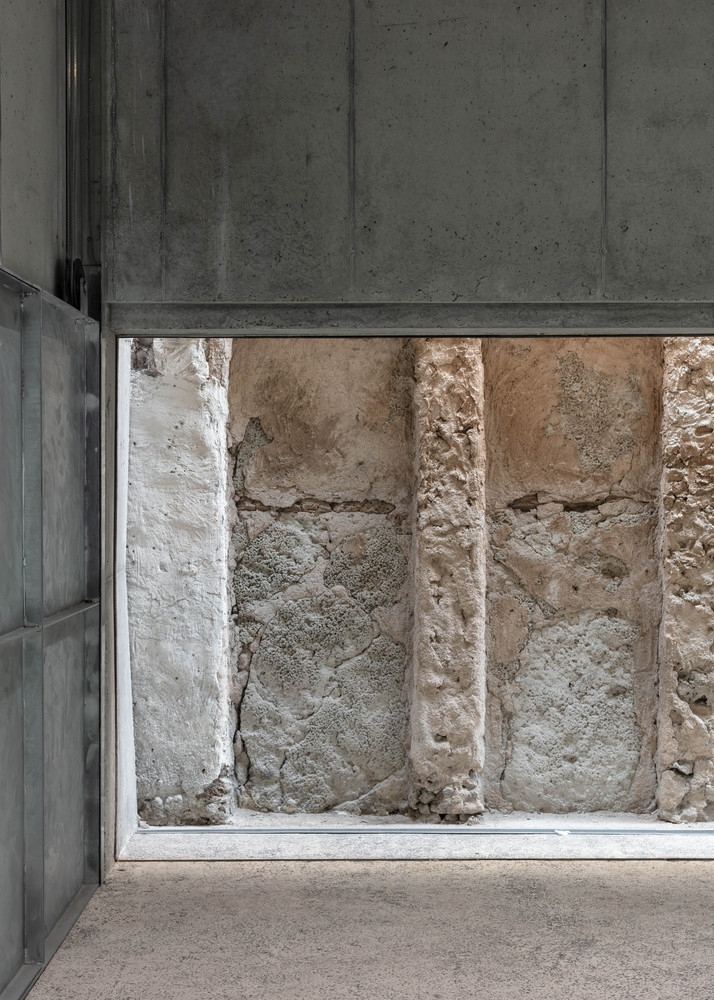 Placeholder reference image: Concrete wall framing a narrow glazed view of rough stone.