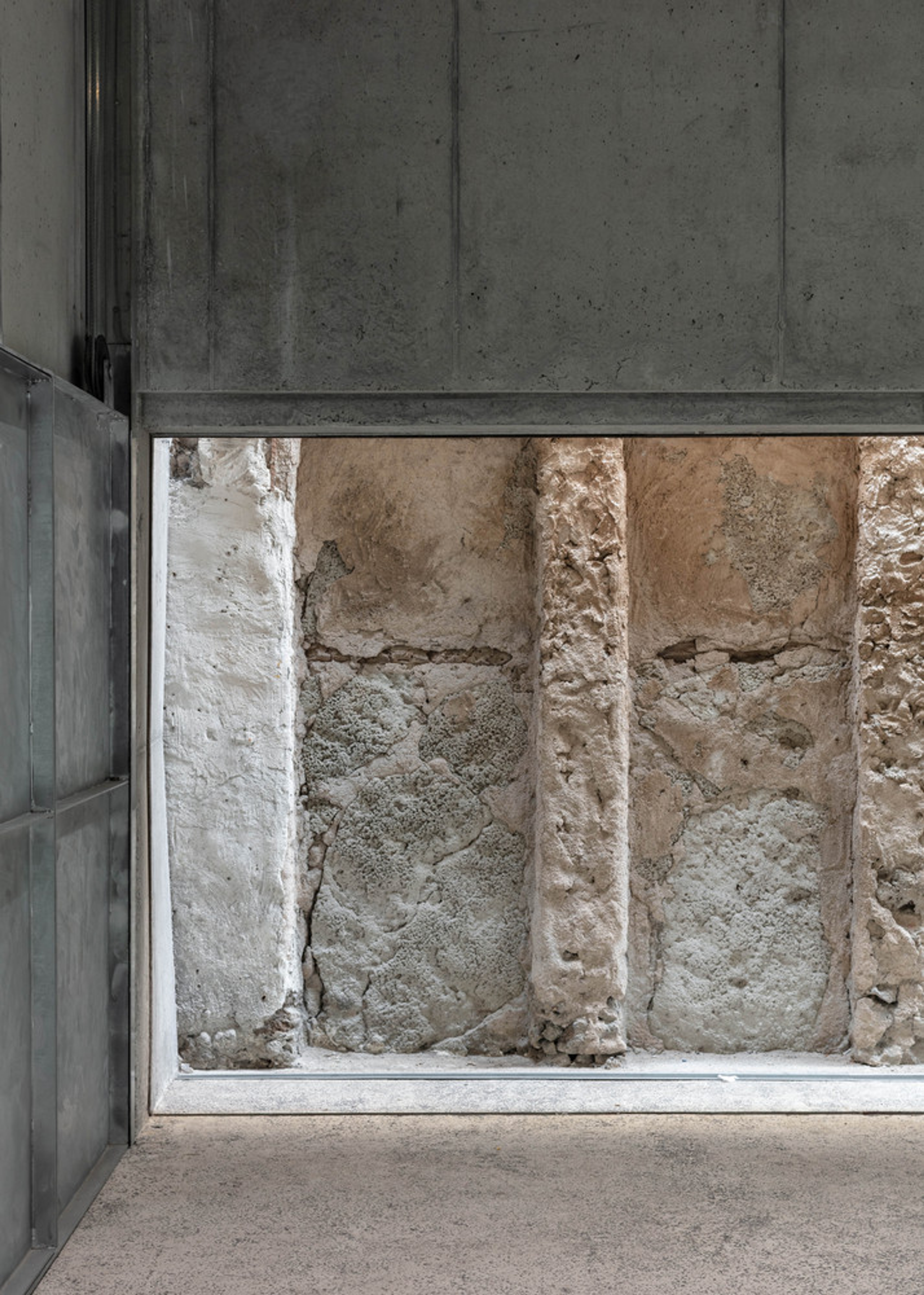 Placeholder reference image: Concrete wall framing a narrow glazed view of rough stone.