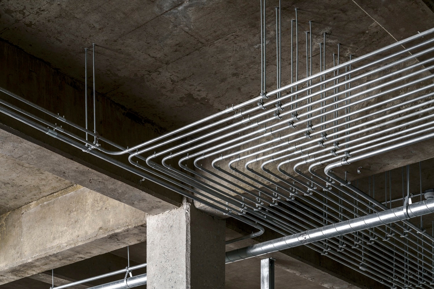 Placeholder reference image: Parallel metal conduits curving beneath an exposed concrete ceiling.