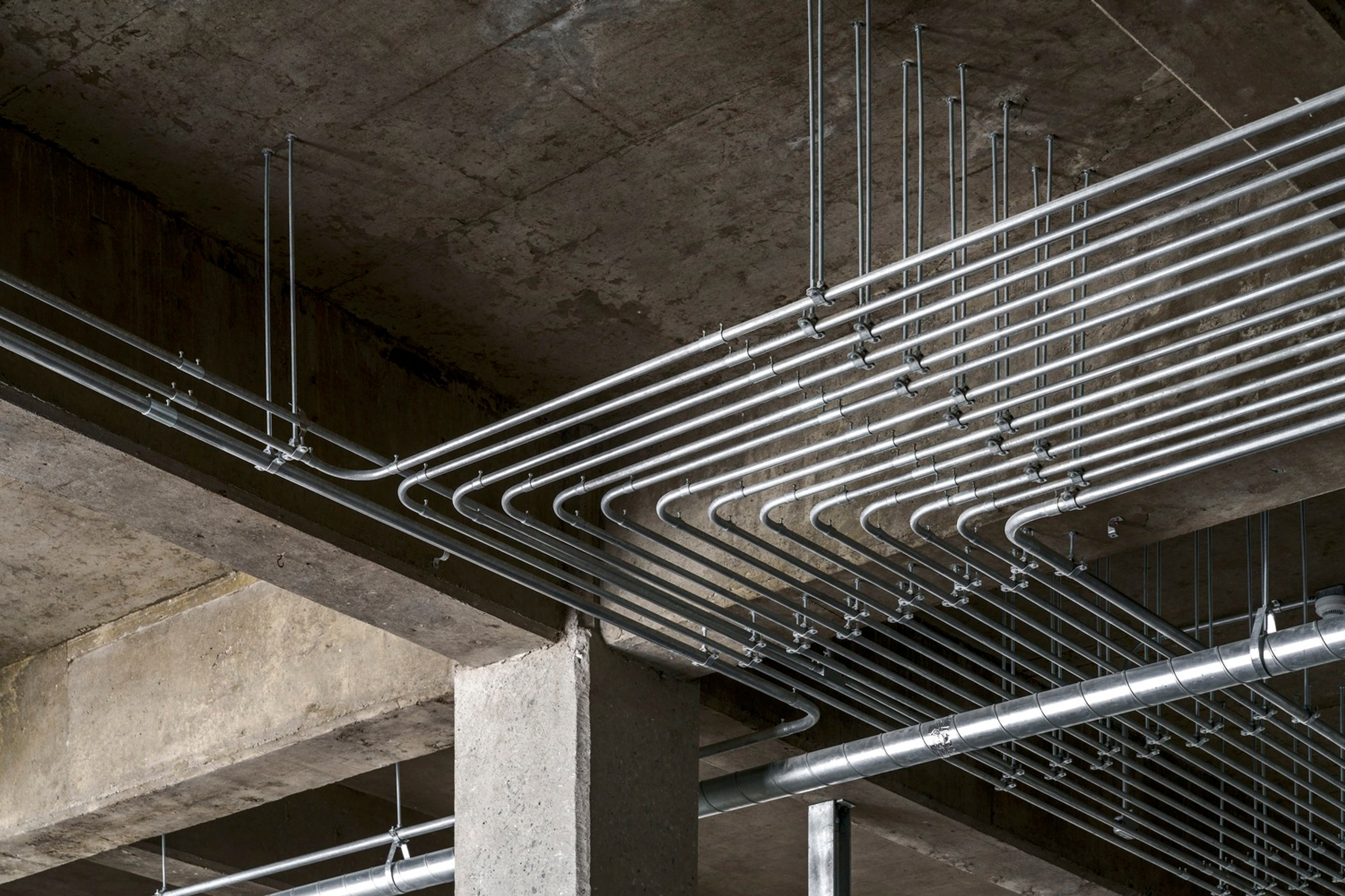 Placeholder reference image: Parallel metal conduits curving beneath an exposed concrete ceiling.