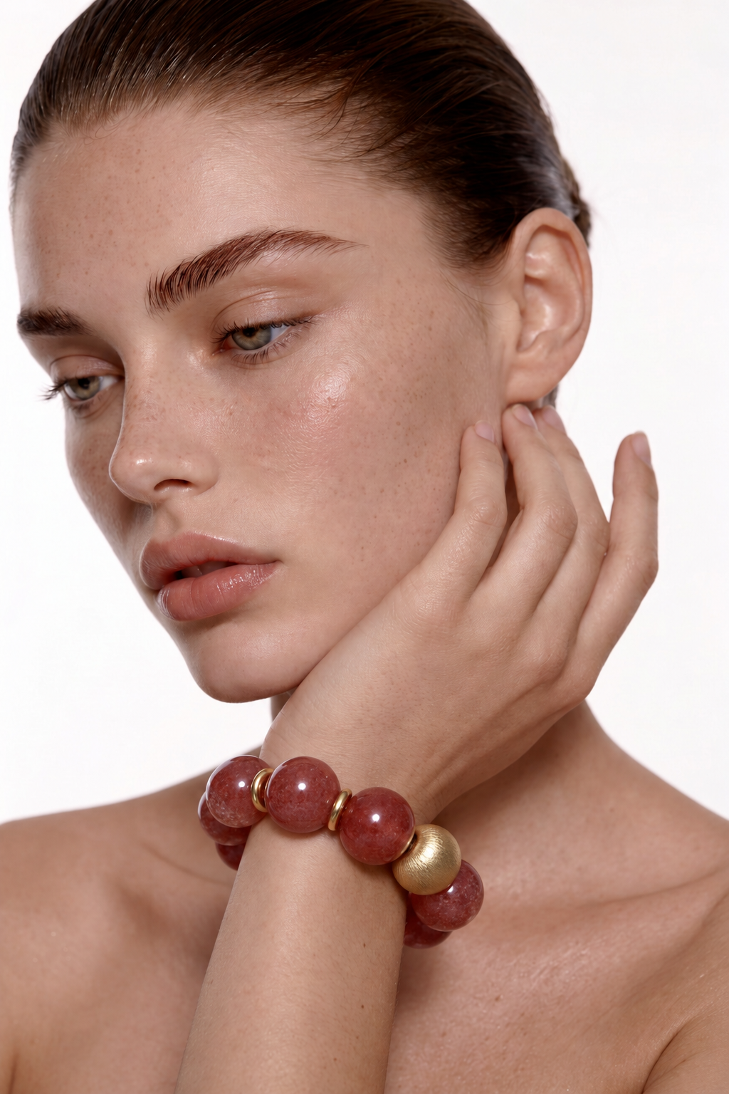 Model wearing the Coral Ember strawberry quartz bracelet, close-up of rose-red beads and brushed gold bead on the wrist