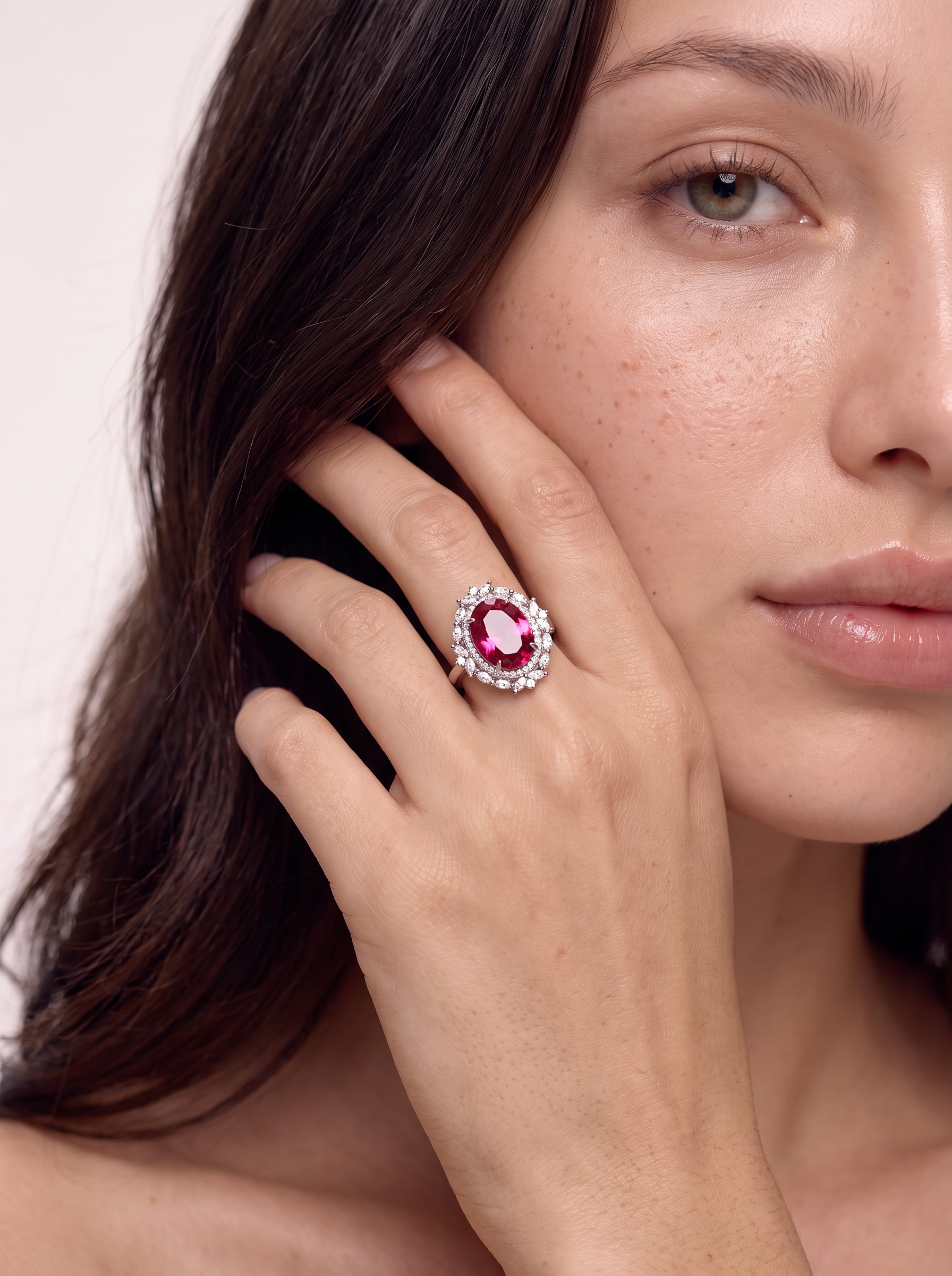 Pink topaz halo ring worn on the finger, hand raised to the face