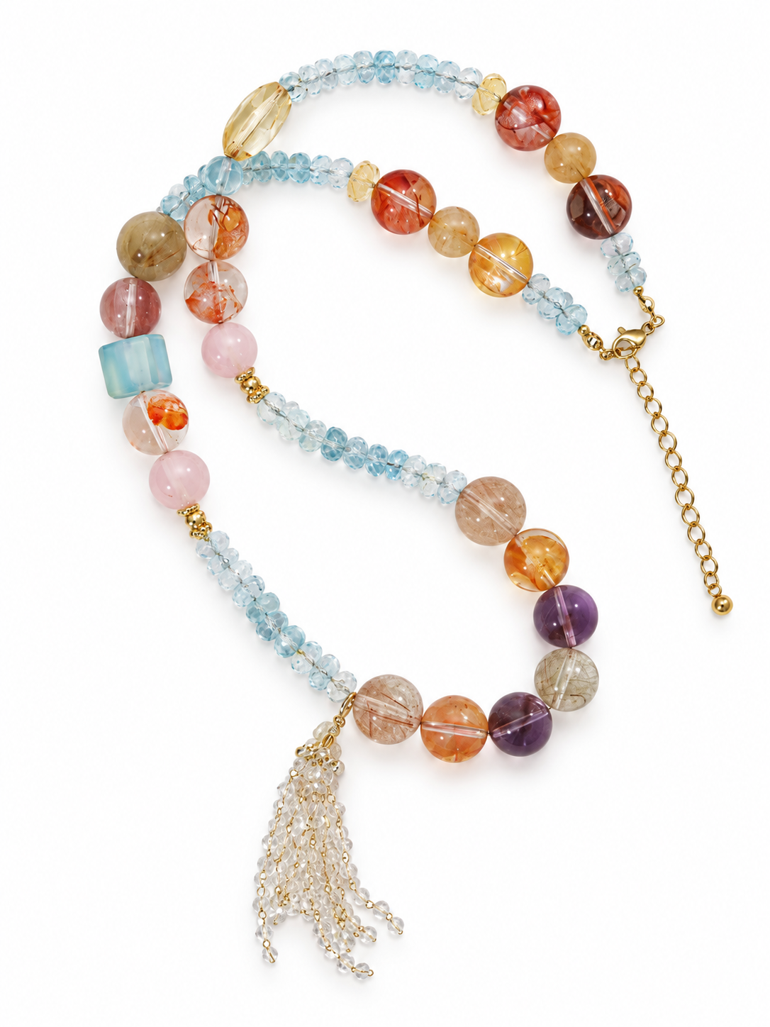 Long multi-crystal necklace with faceted blue topaz rondelles, round hematoid quartz, rose quartz and amethyst beads, a clear quartz tassel and gold extension chain on a white background