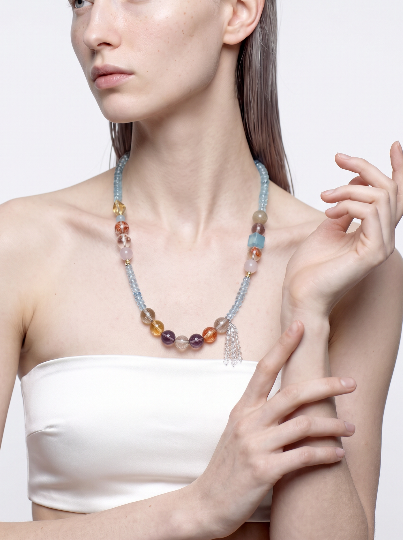 Long blue topaz and crystal necklace worn at the neckline, hand raised