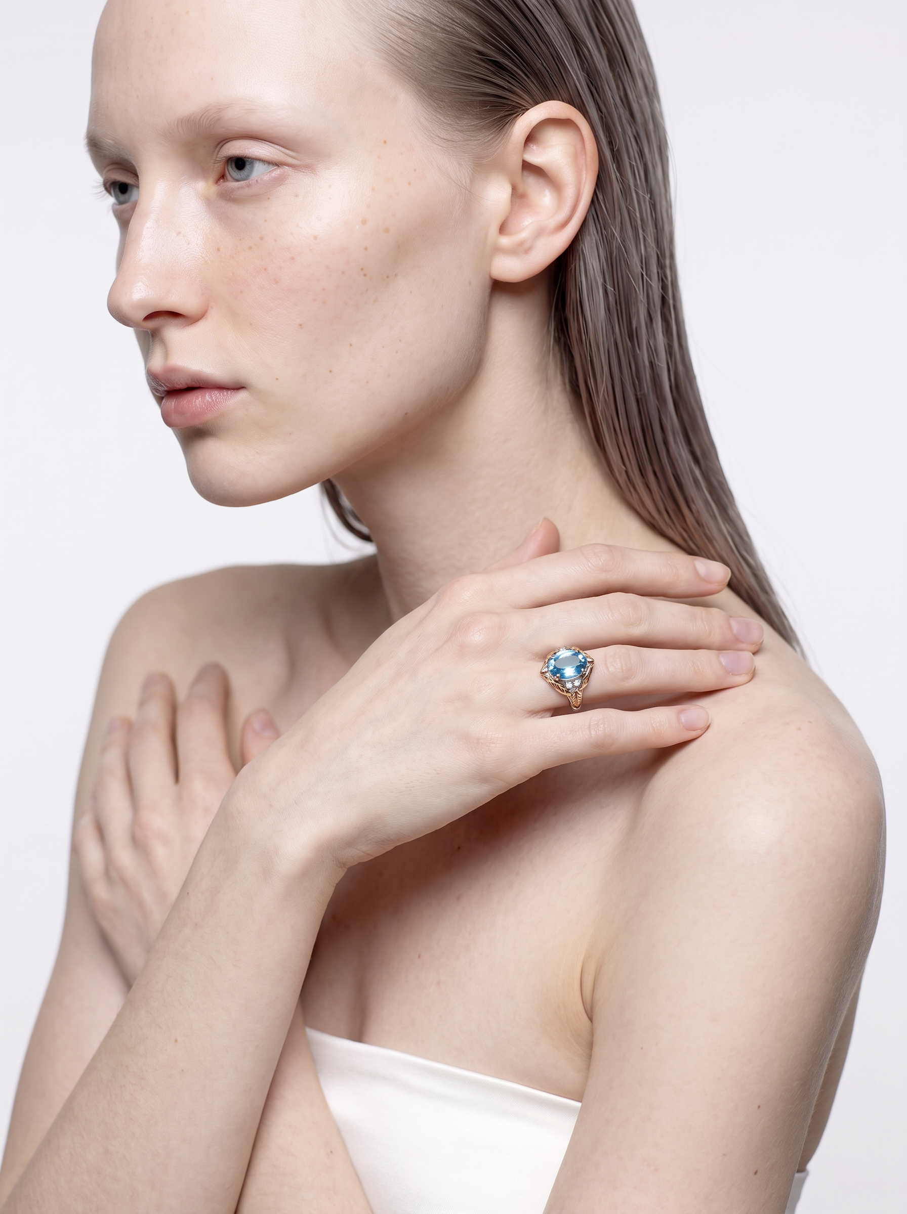 Blue topaz and gold leaf ring worn on the finger, hand resting on the shoulder