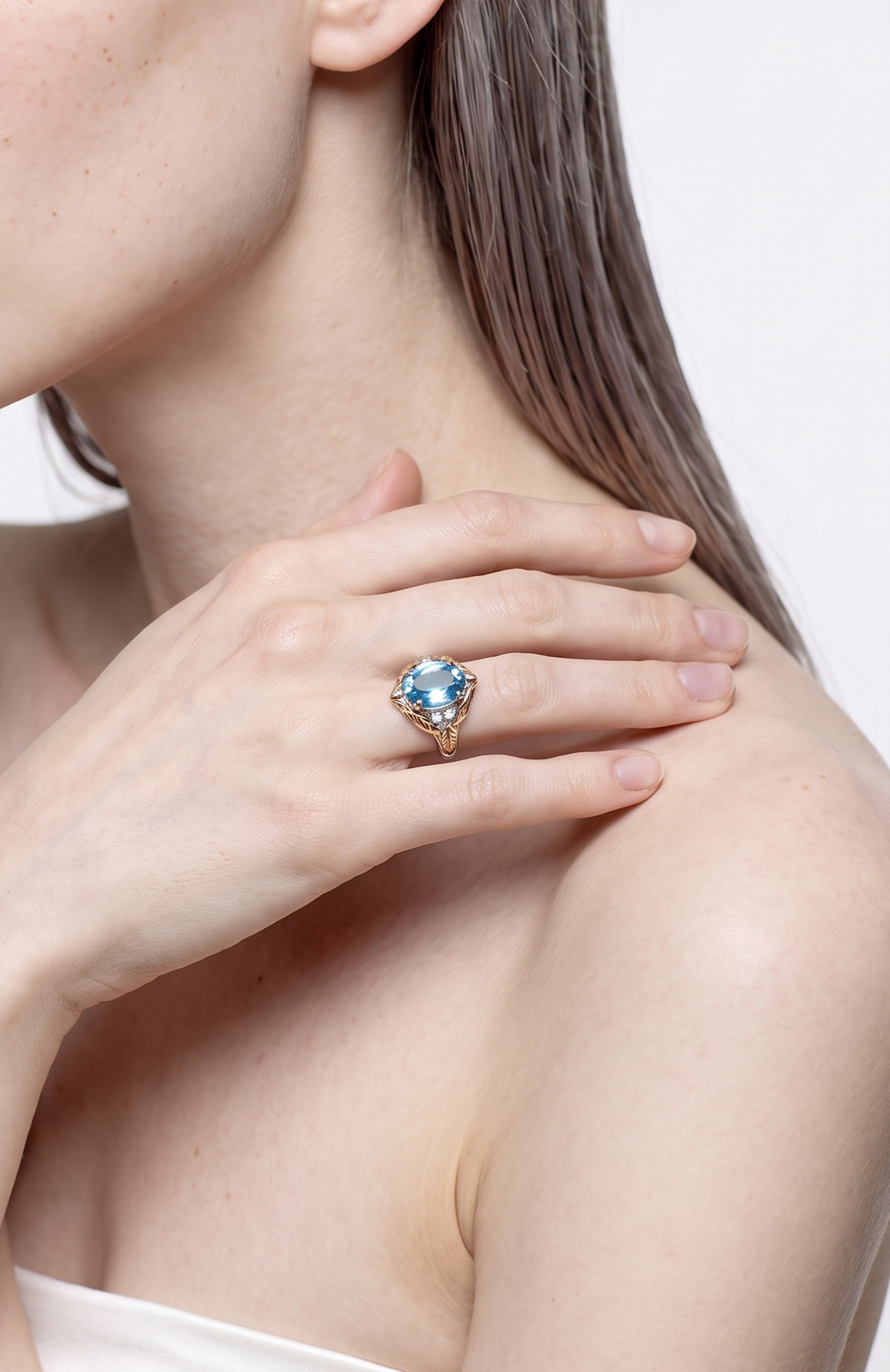 Blue topaz and gold leaf ring worn on the finger, hand resting on the shoulder
