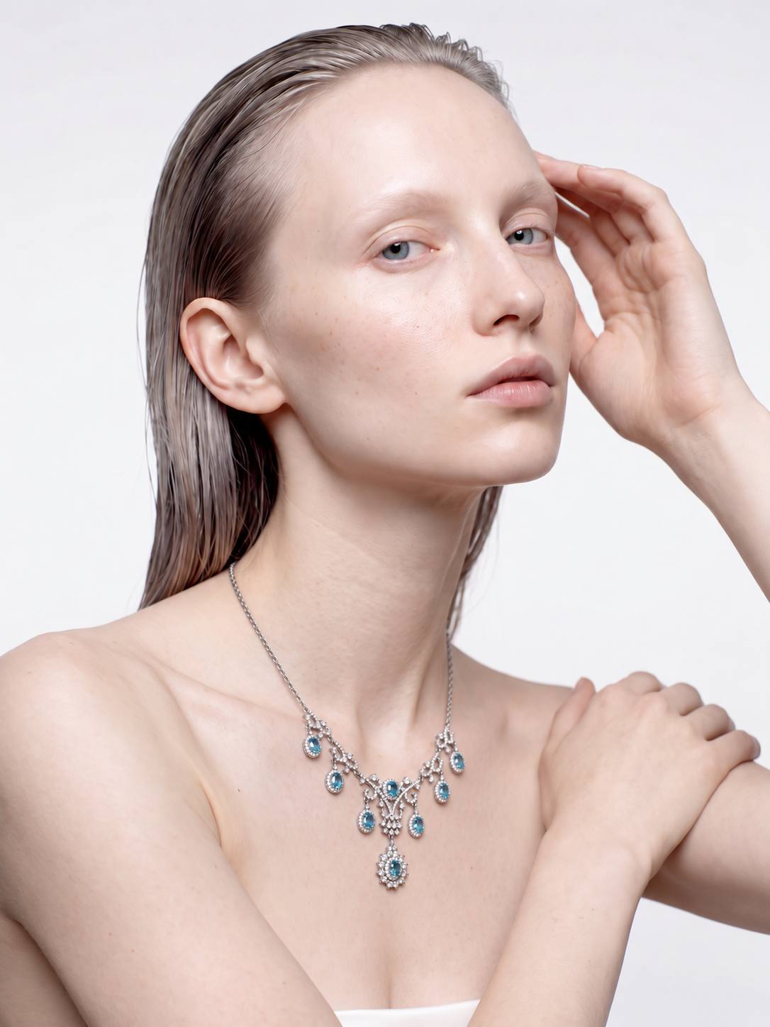 Model wearing the Ocean Gala blue topaz statement necklace, hand raised to the head