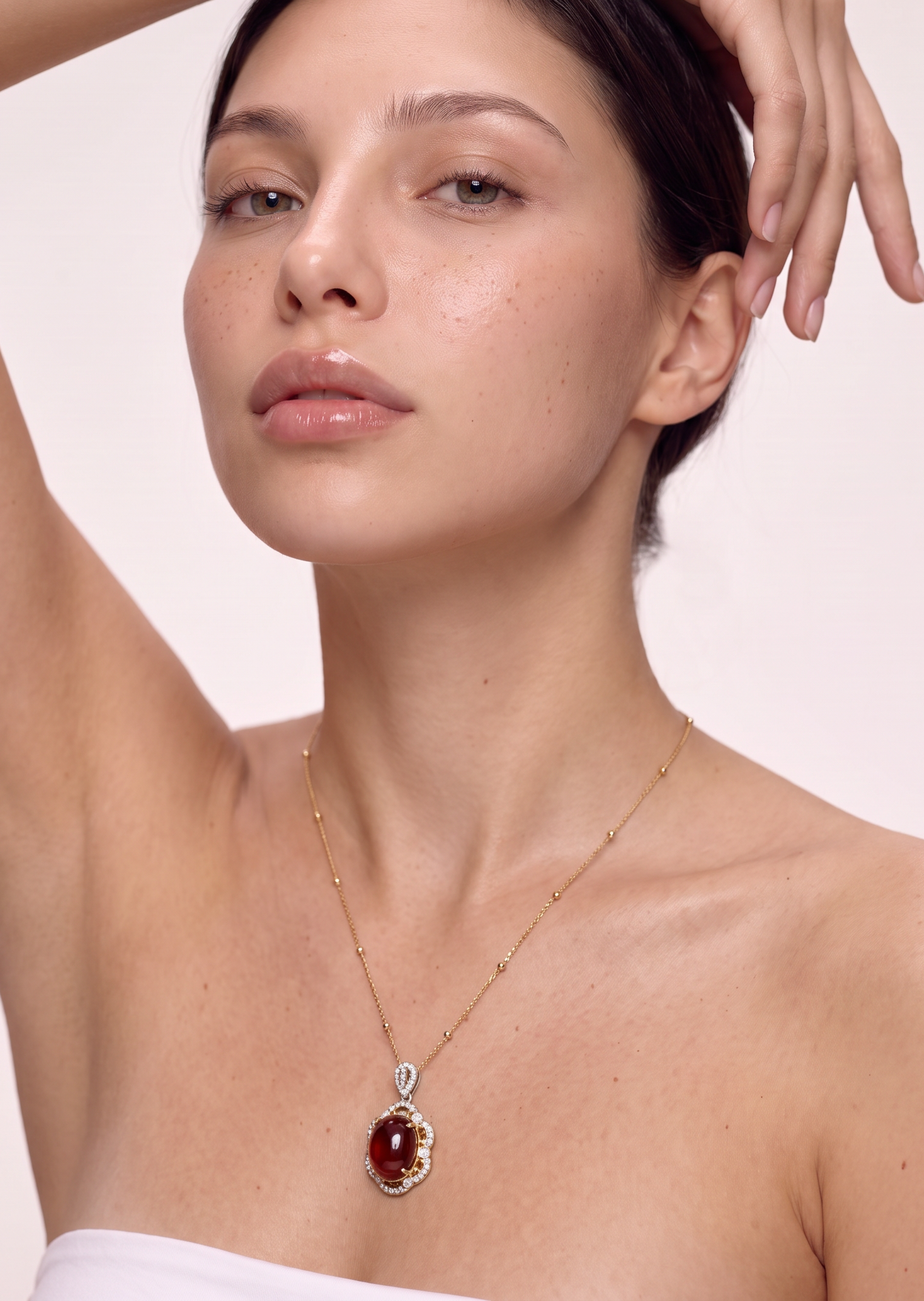 Model wearing the Deep Ember red garnet pendant necklace, arm raised to the head