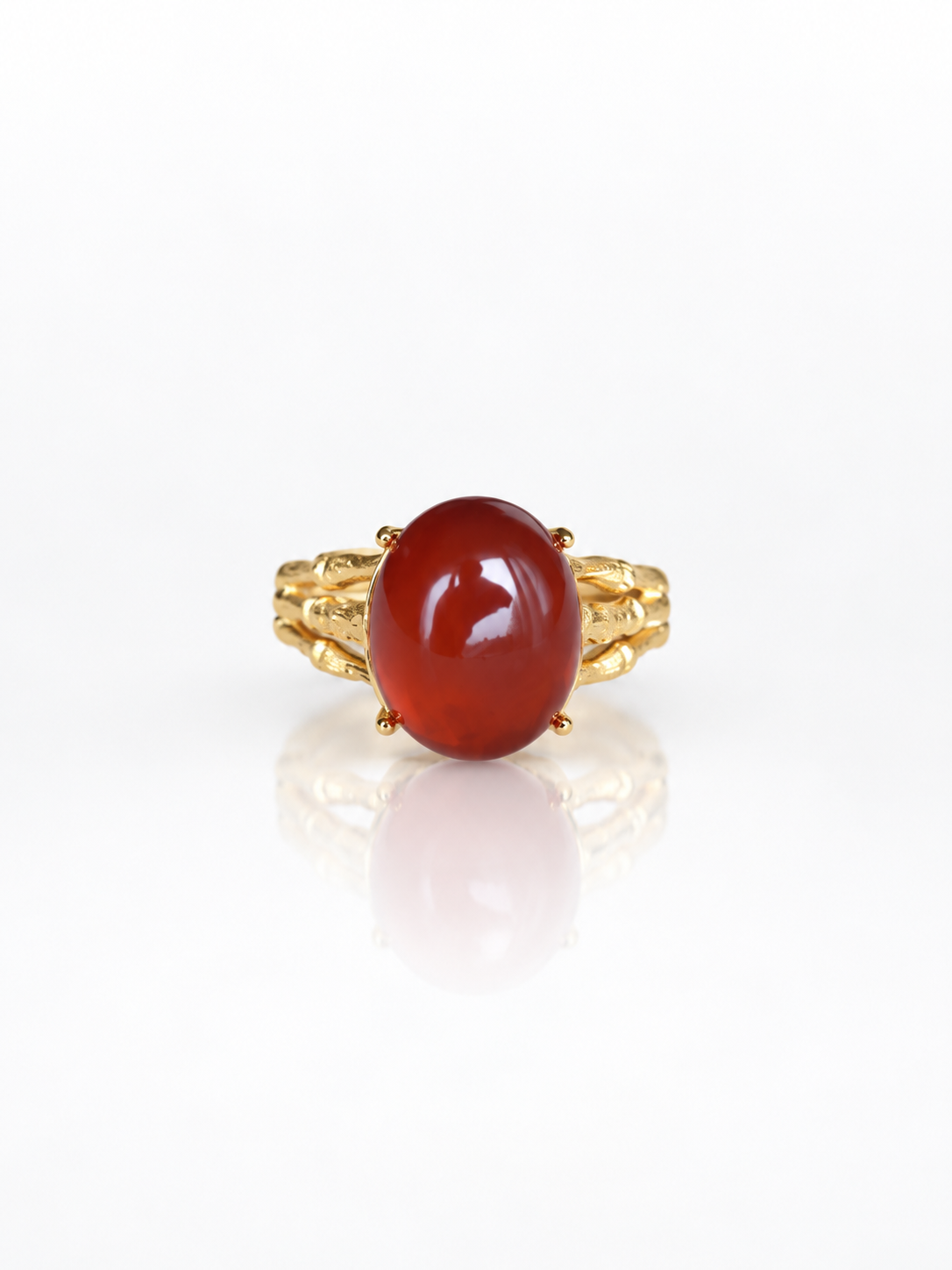 Red garnet cabochon ring on a bamboo-textured gold band on a white background