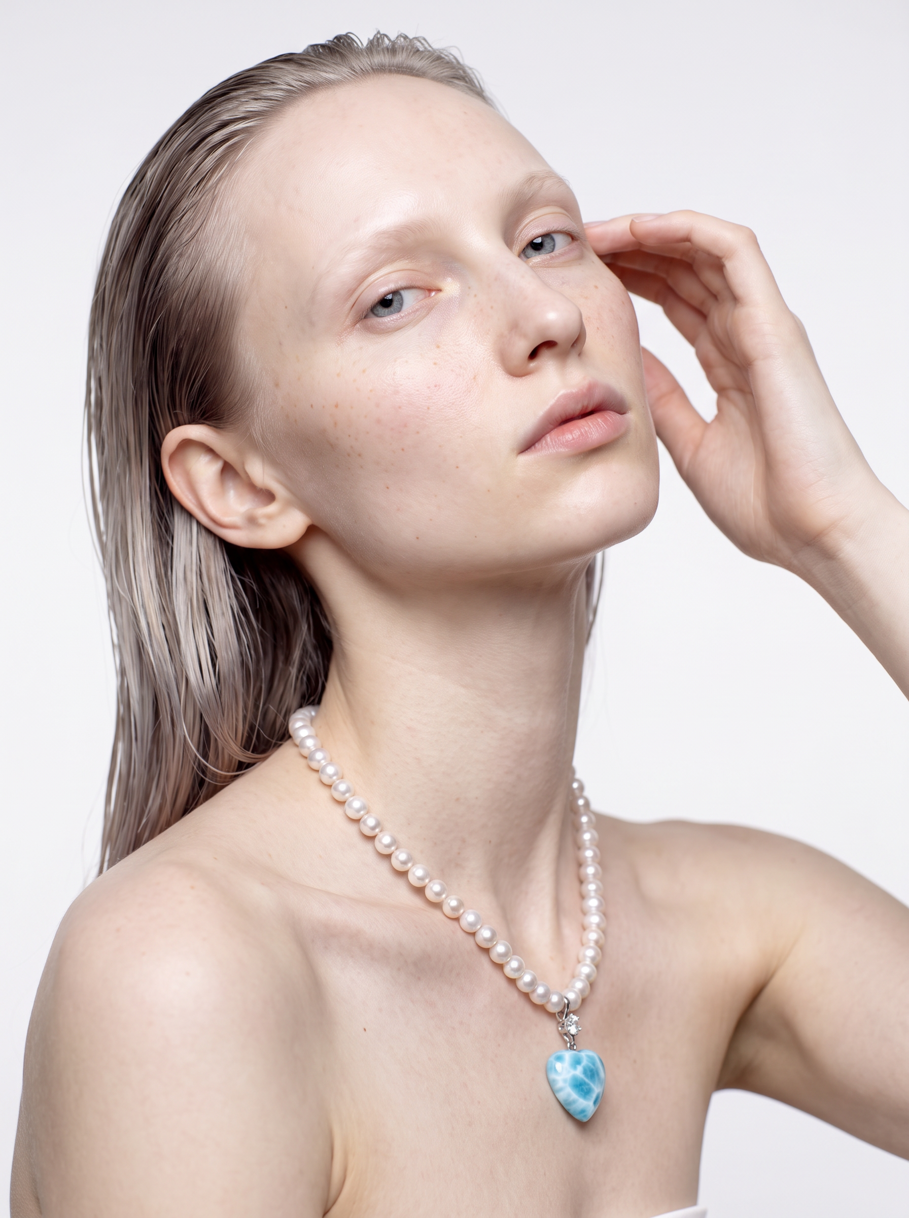 Larimar heart and freshwater pearl necklace worn at the neckline, hand raised to the face