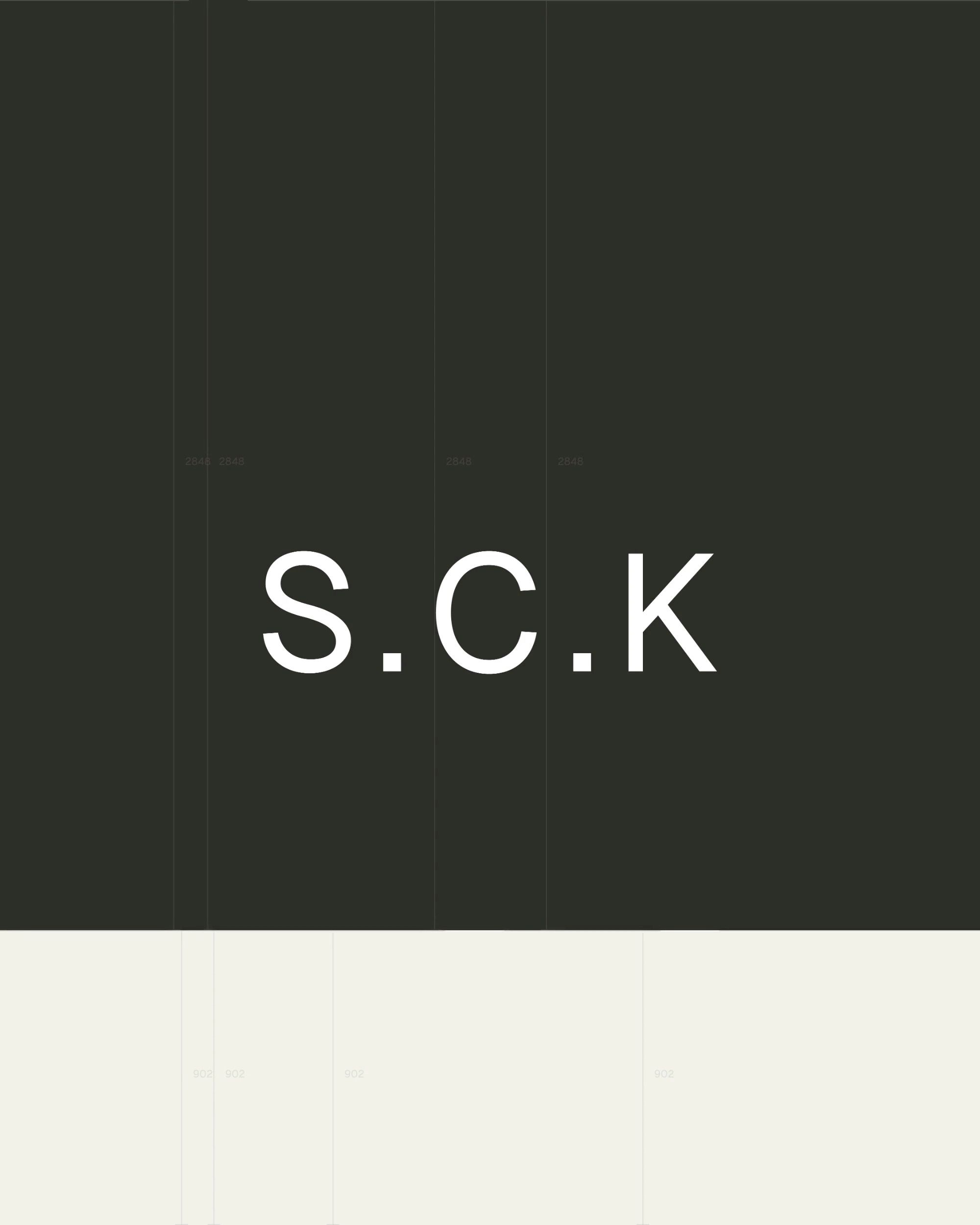 White S.C.K type on charcoal above a cream band, with faint vertical layout guides.