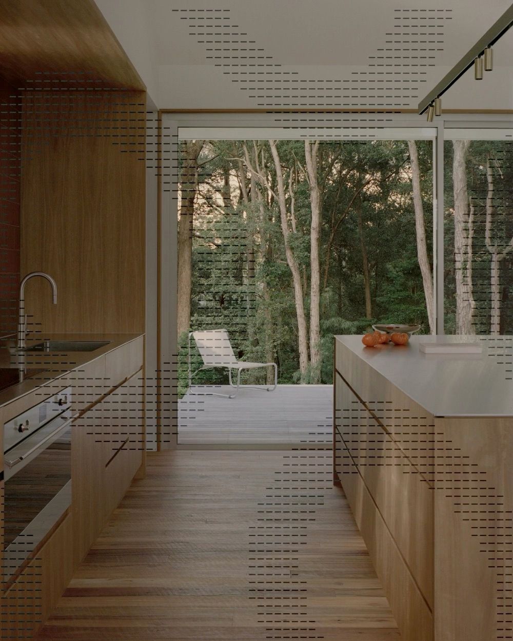 Timber kitchen looking through glass to a deck and forest, overlaid with dashed diagonal shapes.