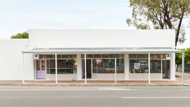 A white brick shopfront with lilac doors and window lettering, seen from across the road.