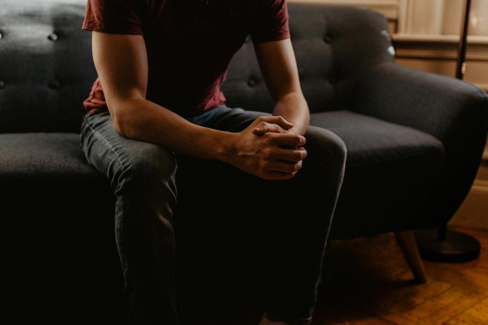 Man in a red shirt sitting on a couch with his hands together, looking relaxed