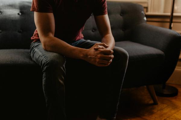Man in a red shirt sitting on a couch with his hands together, looking relaxed