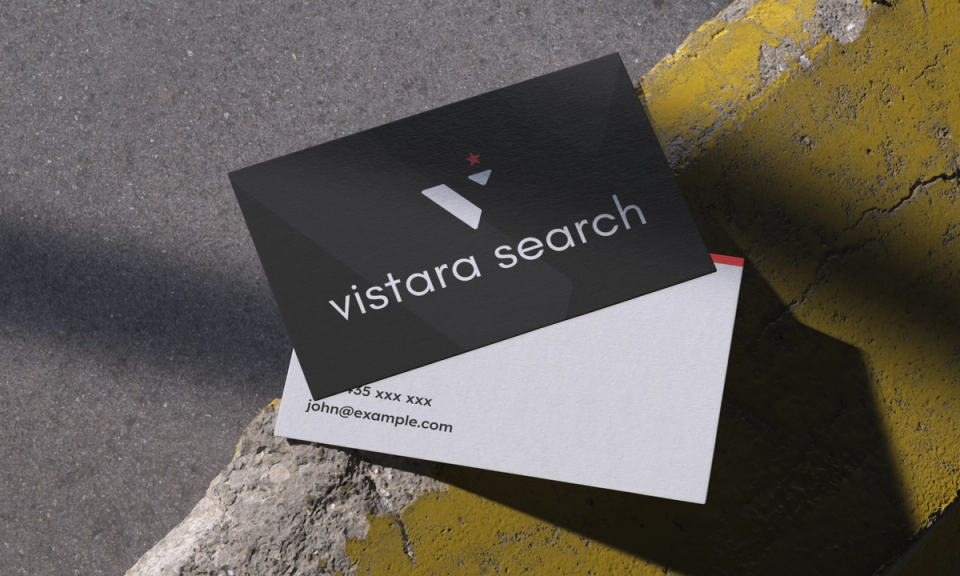 Vistara Search business cards: a black card with the silver logo and wordmark over a white card with contact details, on yellow-painted concrete