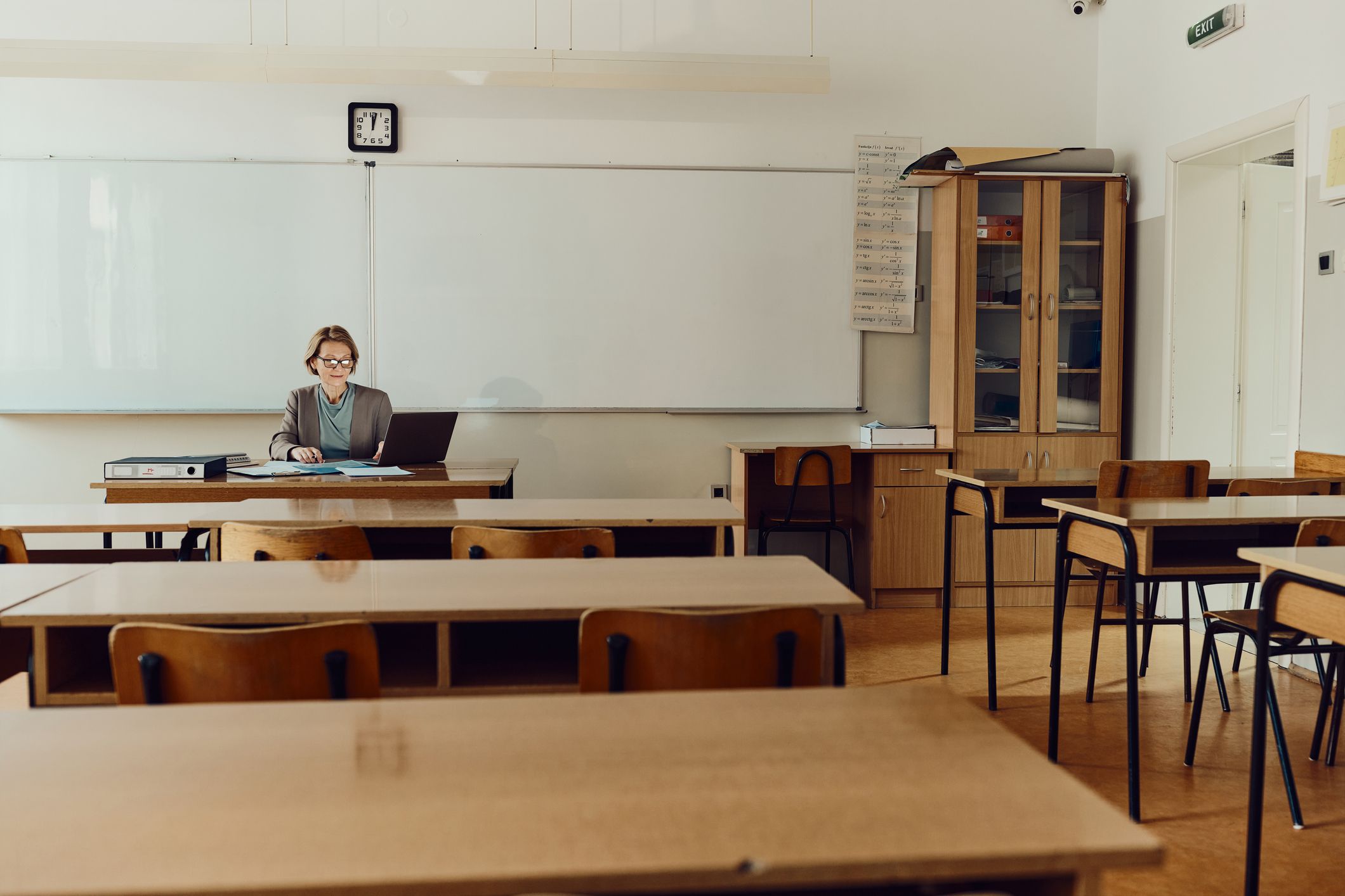 En lærer sitter og retter prøver ved kateteret i et klasserom. Bilde.