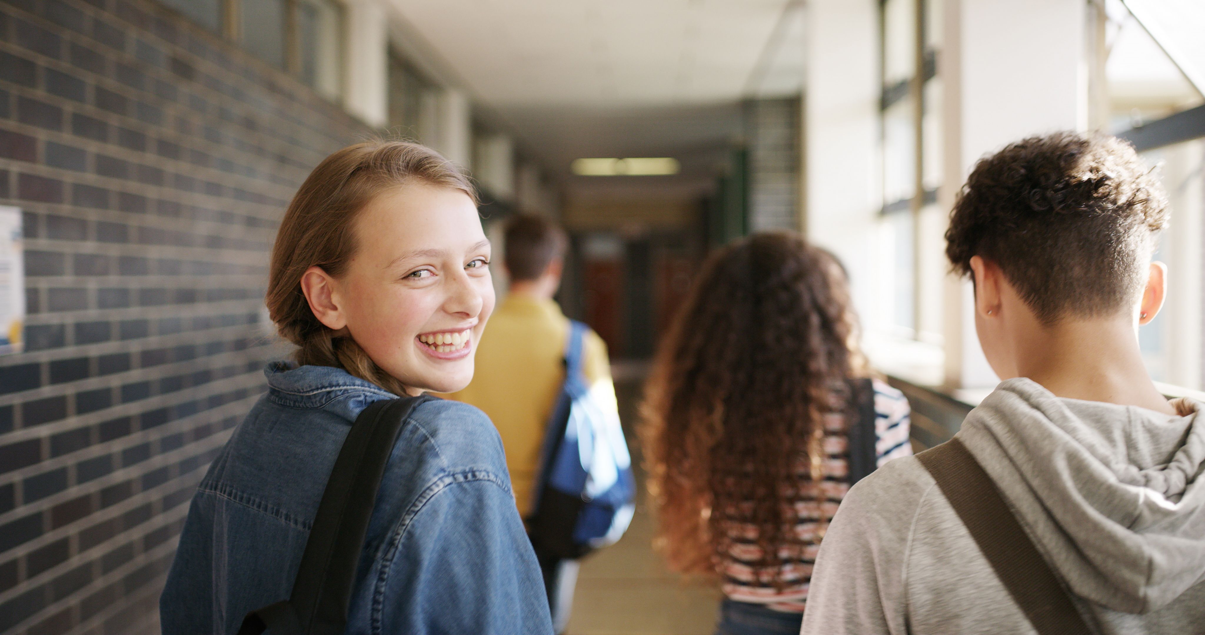 En tenåringsjente går i gangen på skolen med noen venner. Bilde.