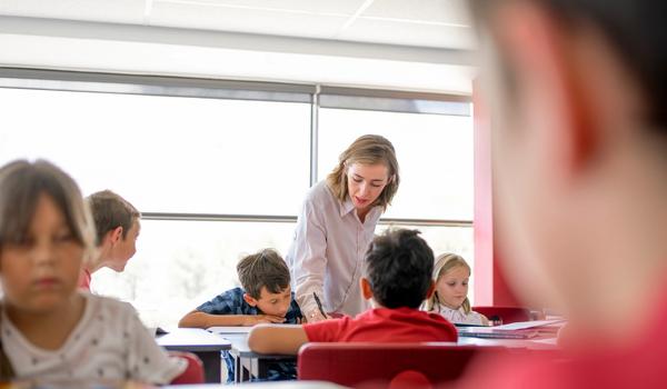 En lærer hjelper en elev med å skrive. Bilde.