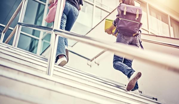 To elever går opp en trapp til skolens hovedinngang. Bilde.