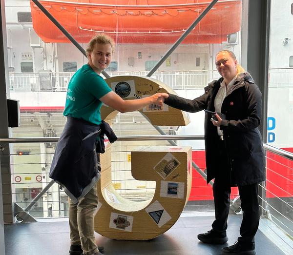 En lektorstudent overrekker en 1,5 meter høy G til en ansatt på Hurtigruten i Bergen.