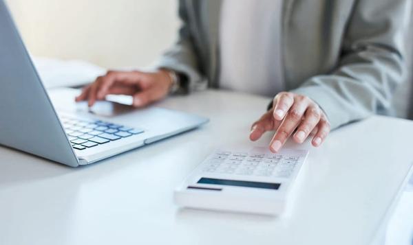 Noen som regner ut noe med kalkulator og bærbar pc på et bord.