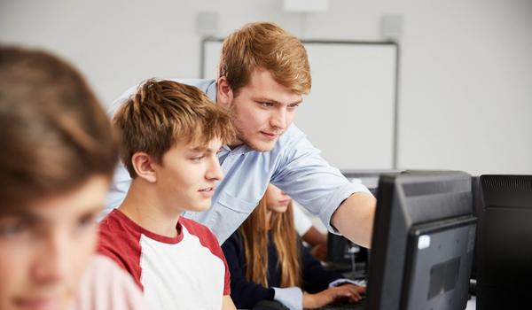 En videregåendeelev får hjelp med noe på en pc-skjerm av en lærer.