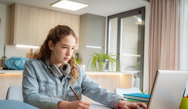 En videregåendeelev skriver på en oppgave hjemme. Bilde.
